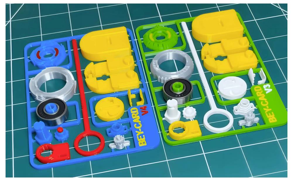 Zwei LEGO-ähnliche Spritzgussrahmen mit den Aufschriften „BEYCARD V1" und „BETACARD V3" mit verschiedenfarbigen Kunststoffteilen, die in Fächern auf einer Schneidematte angeordnet sind.