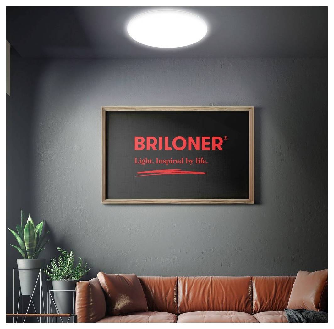An der Wand befestigtes gerahmtes BRILONER-Schild mit dem Slogan „Licht. Inspiriert vom Leben." über einem braunen Ledersofa in einem modernen Wohnzimmer.
