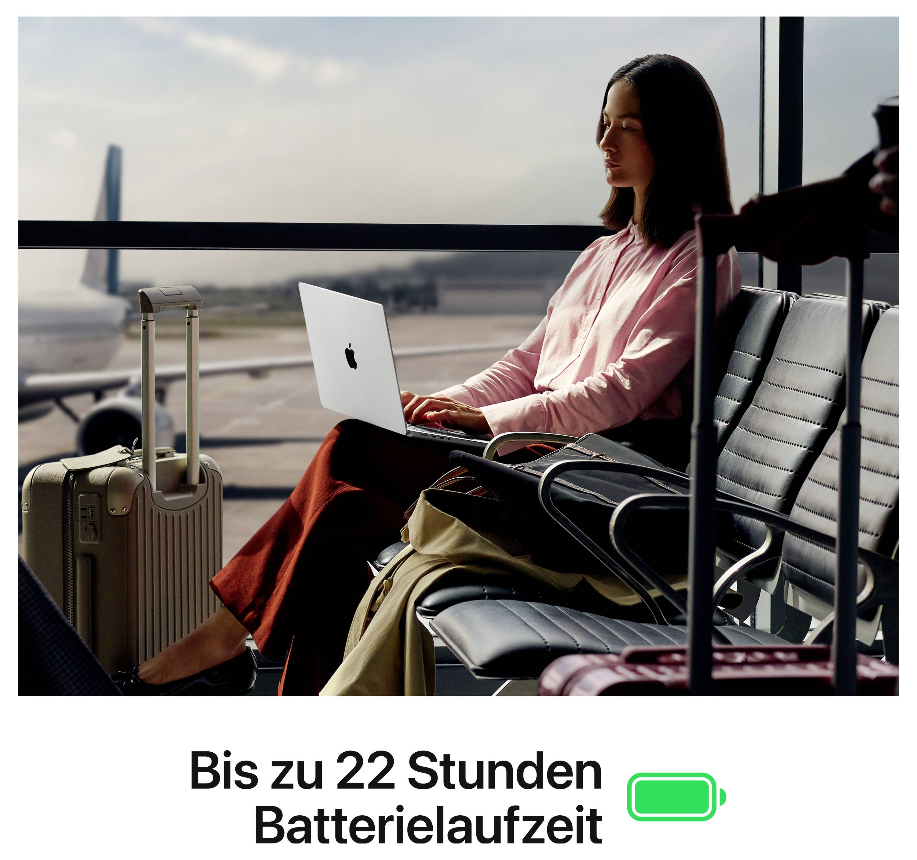Reisende arbeitet mit Laptop am Flughafen; daneben Koffer. Unten steht 'Bis zu 22 Stunden Batterielaufzeit'.