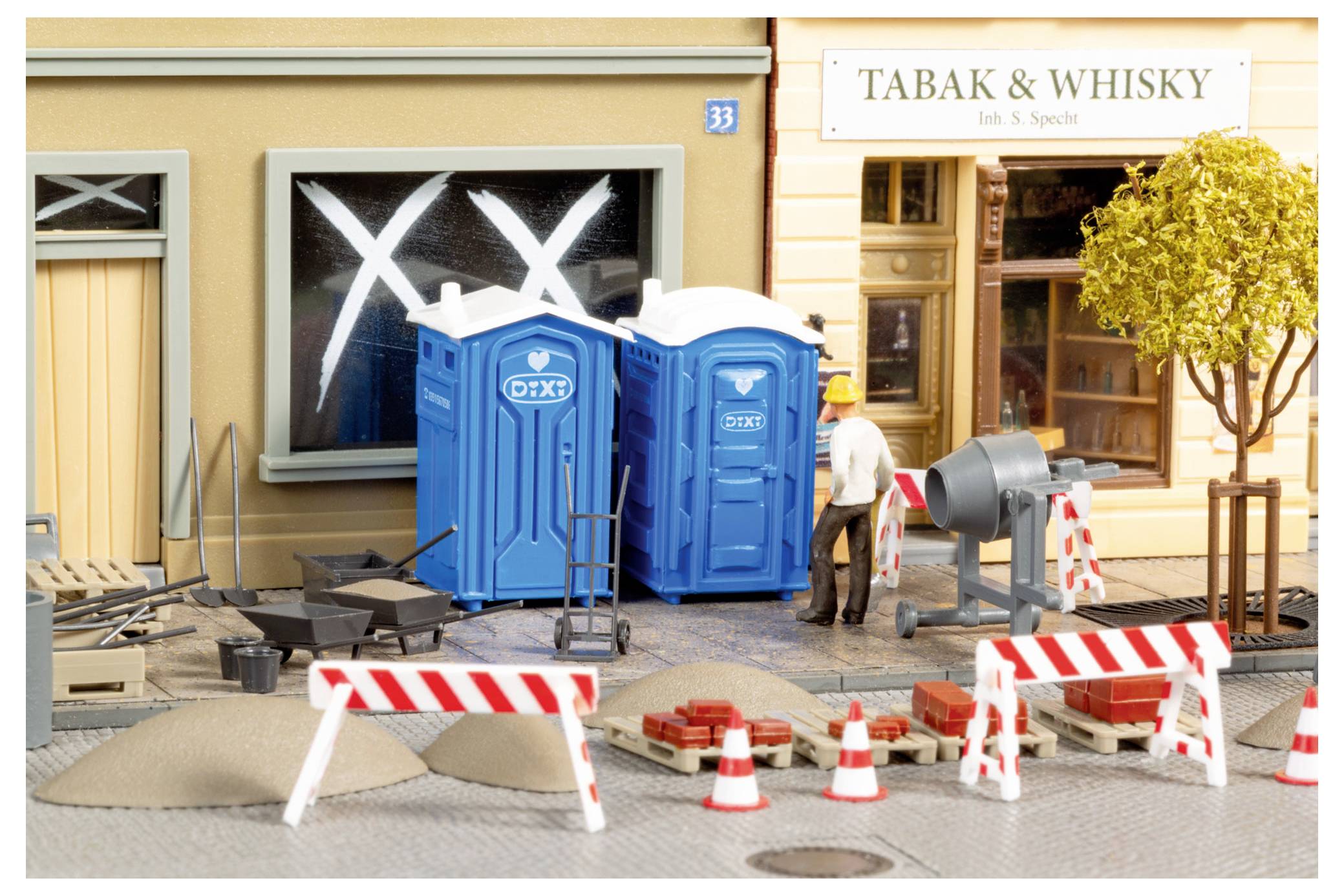 Miniatur-Straßenbauszene mit zwei blauen tragbaren Toiletten, Straßenbaubarrieren, Verkehrskegeln und einem Arbeiter vor einem Geschäft mit der Aufschrift „TABAK & WHISKY".