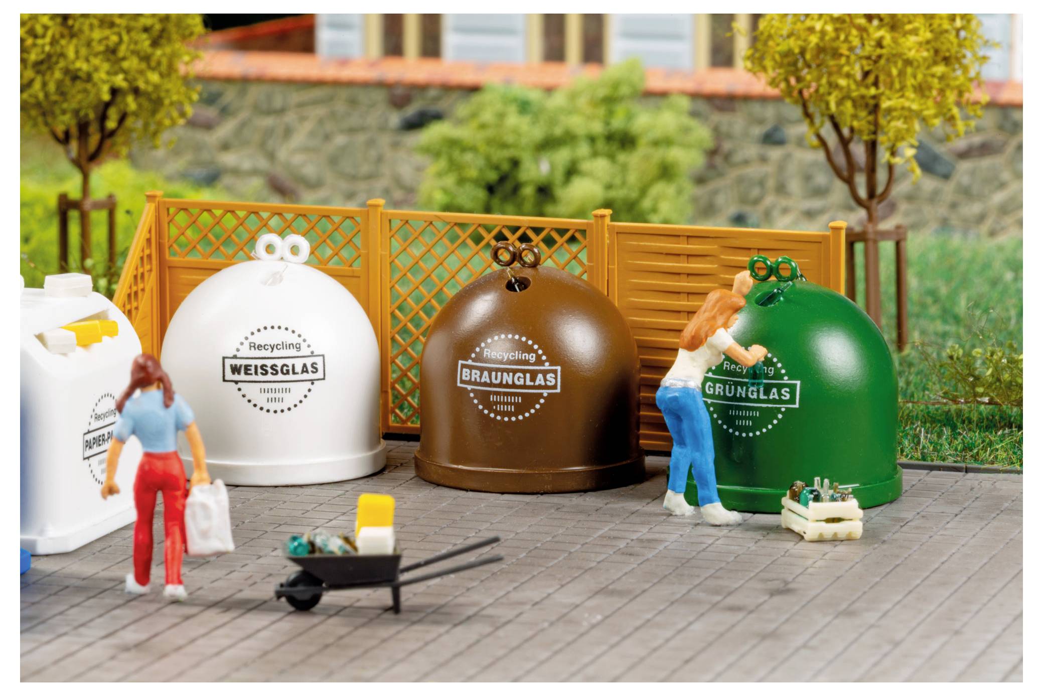 Winzige Menschen sortieren Glasflaschen in farblich gekennzeichnete Recyclingbehälter mit den Aufschriften „WEISSGLAS", „BRAUNGLAS" und „GRÜNGLAS" neben einem Zaun.