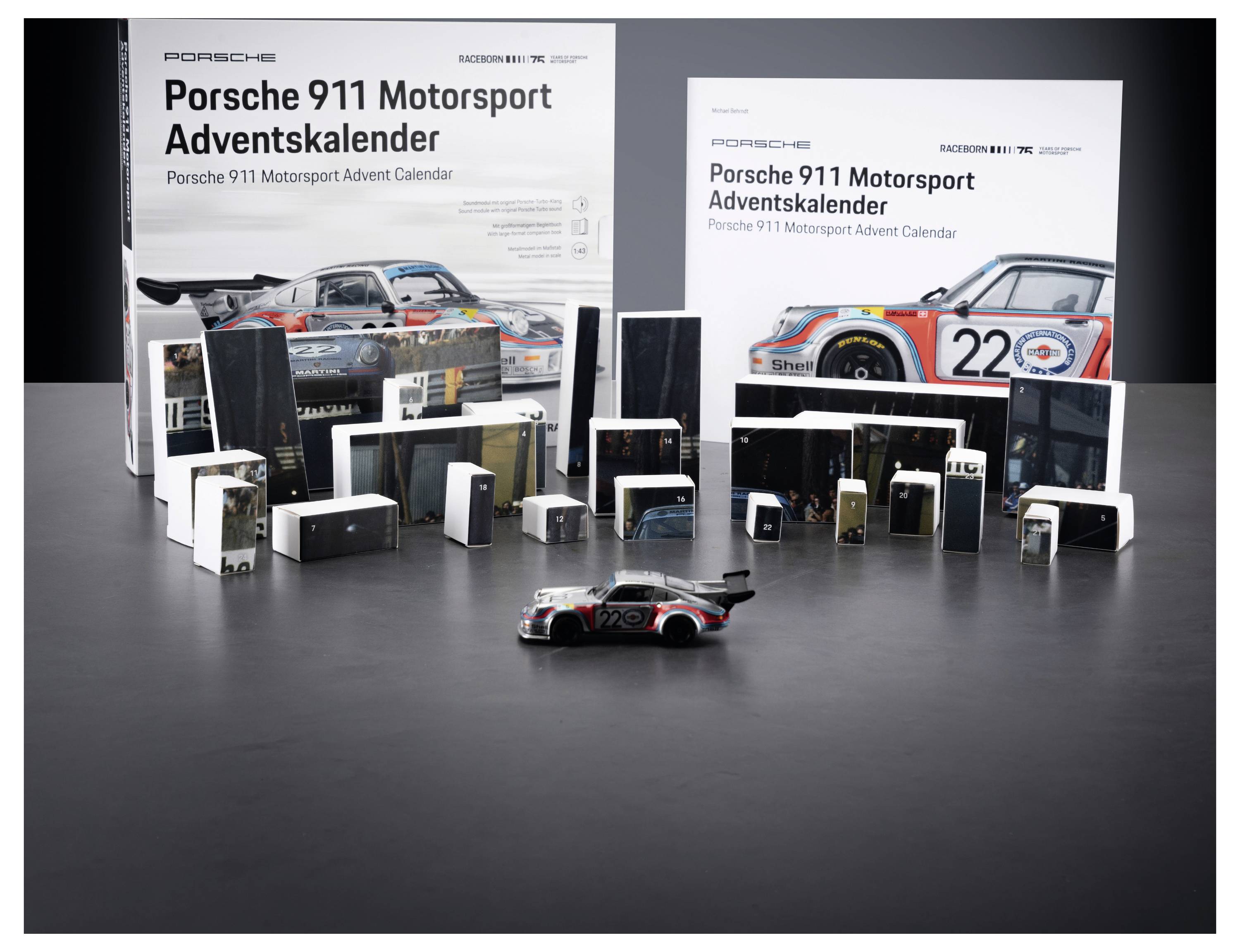 Porsche 911 Motorsport Adventskalender Display mit zwei großen Boxen, vielen kleinen nummerierten Paketen und einem Miniatur-Porsche Rennwagen vorne.