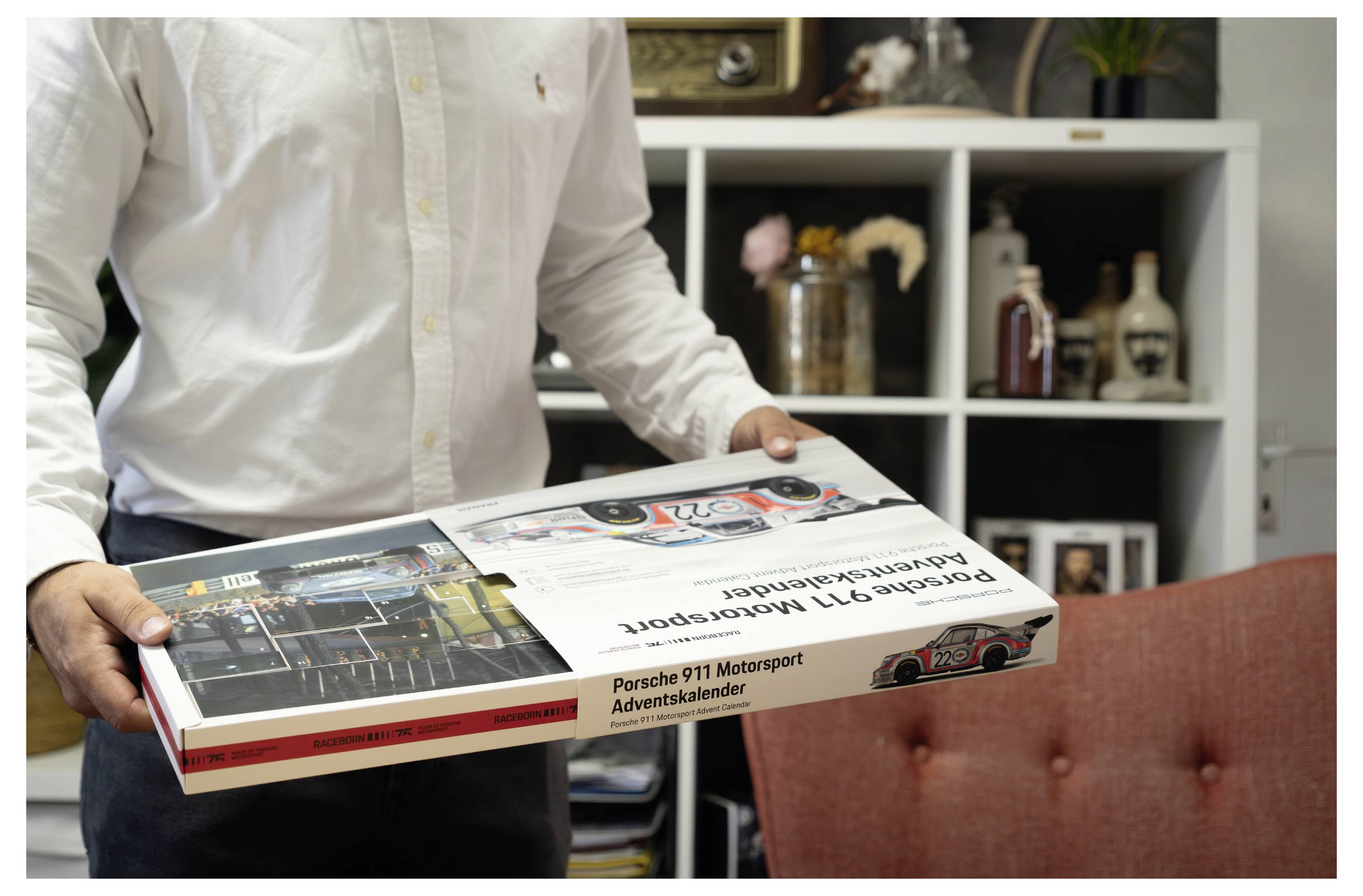 Person, die eine Porsche 911 Motorsport Adventskalender-Box in einem Wohnzimmer hält und die Produktverpackung und das Etikett zeigt.