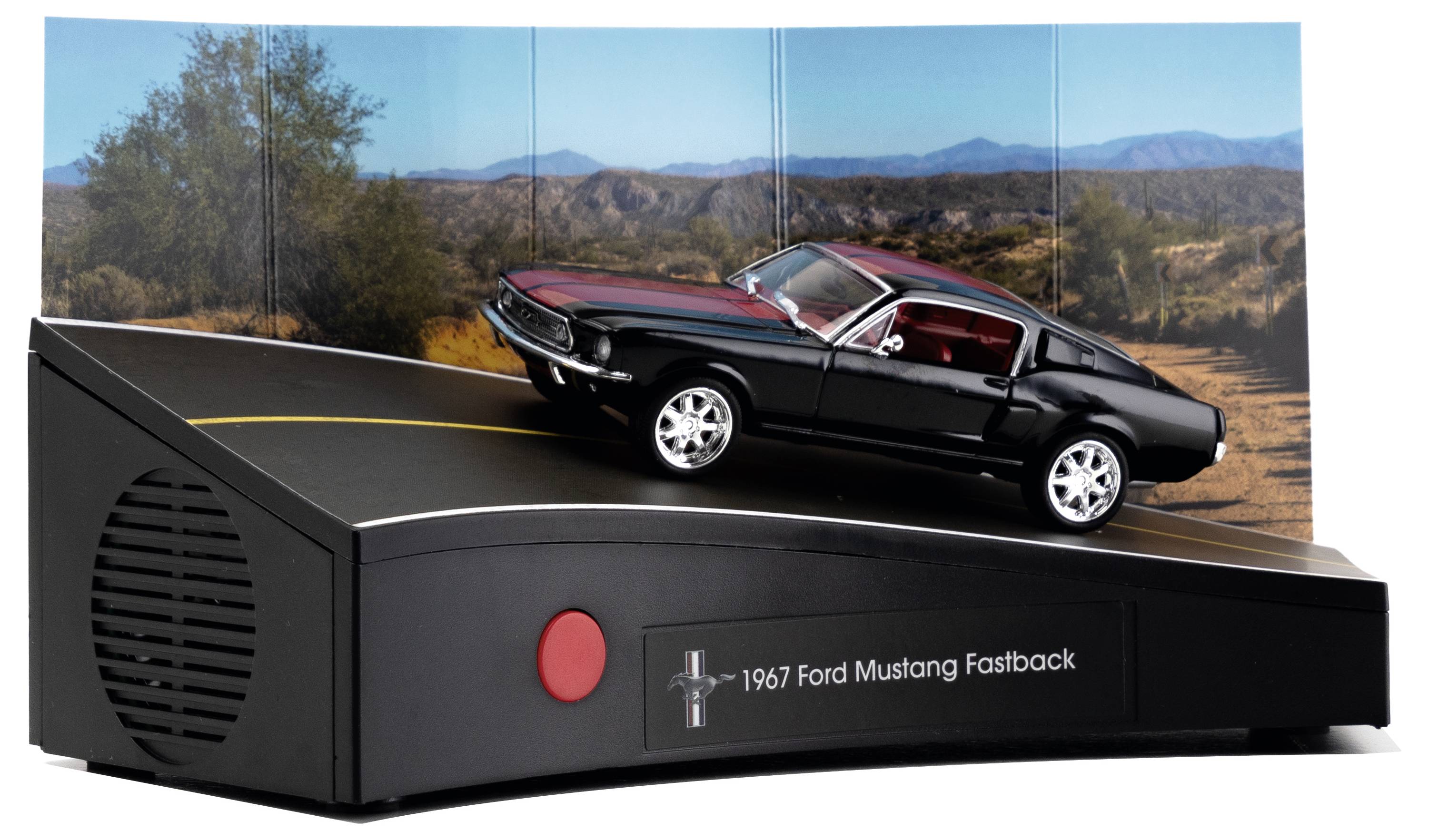 Modell 1967 Ford Mustang Fastback auf schwarzem Sockel mit rotem Knopf präsentiert, vor einer malerischen Bergkulisse.
