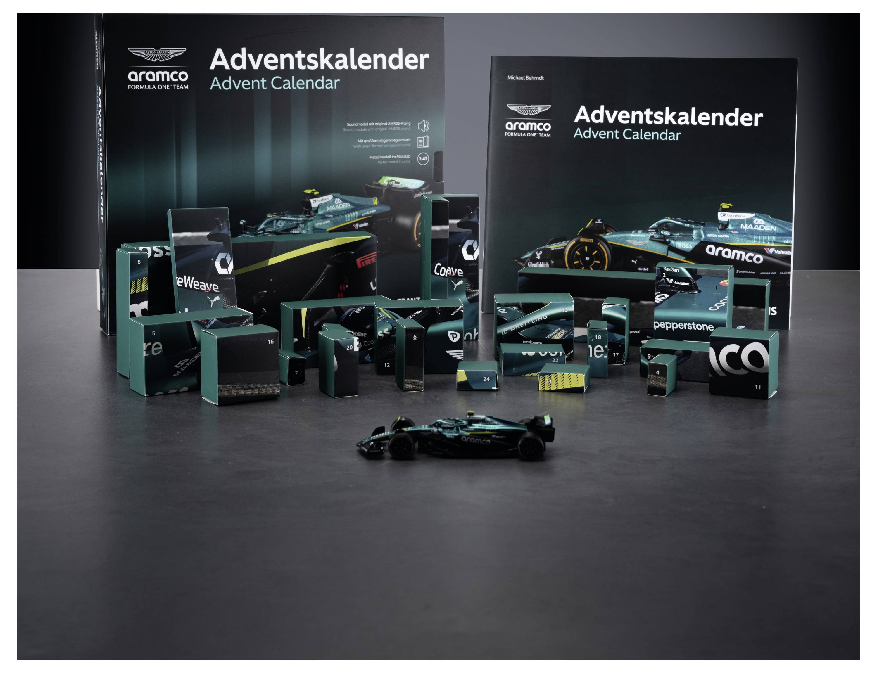 Zwei Aramco-"Adventskalender"-Boxen und ein kleines Formel-1-Modellauto mit nummerierten Fächern in Blaugrün und Schwarz, die über einen Tisch verteilt sind.
