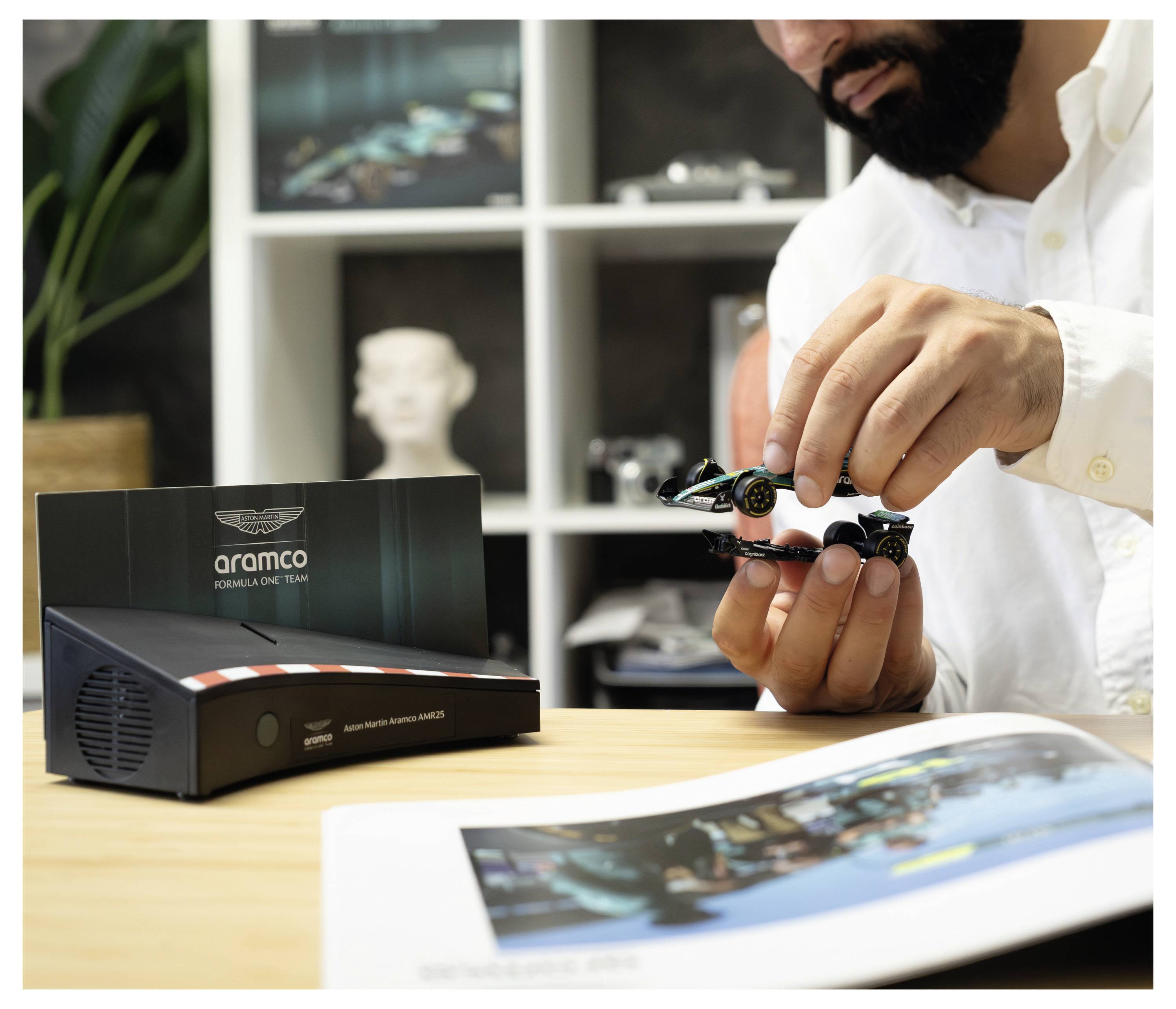 Ein Mann, der neben einer "Aramco"-Ausstellungsbox an einem Schreibtisch ein kleines Formel-1-Modellauto zusammenbaut.