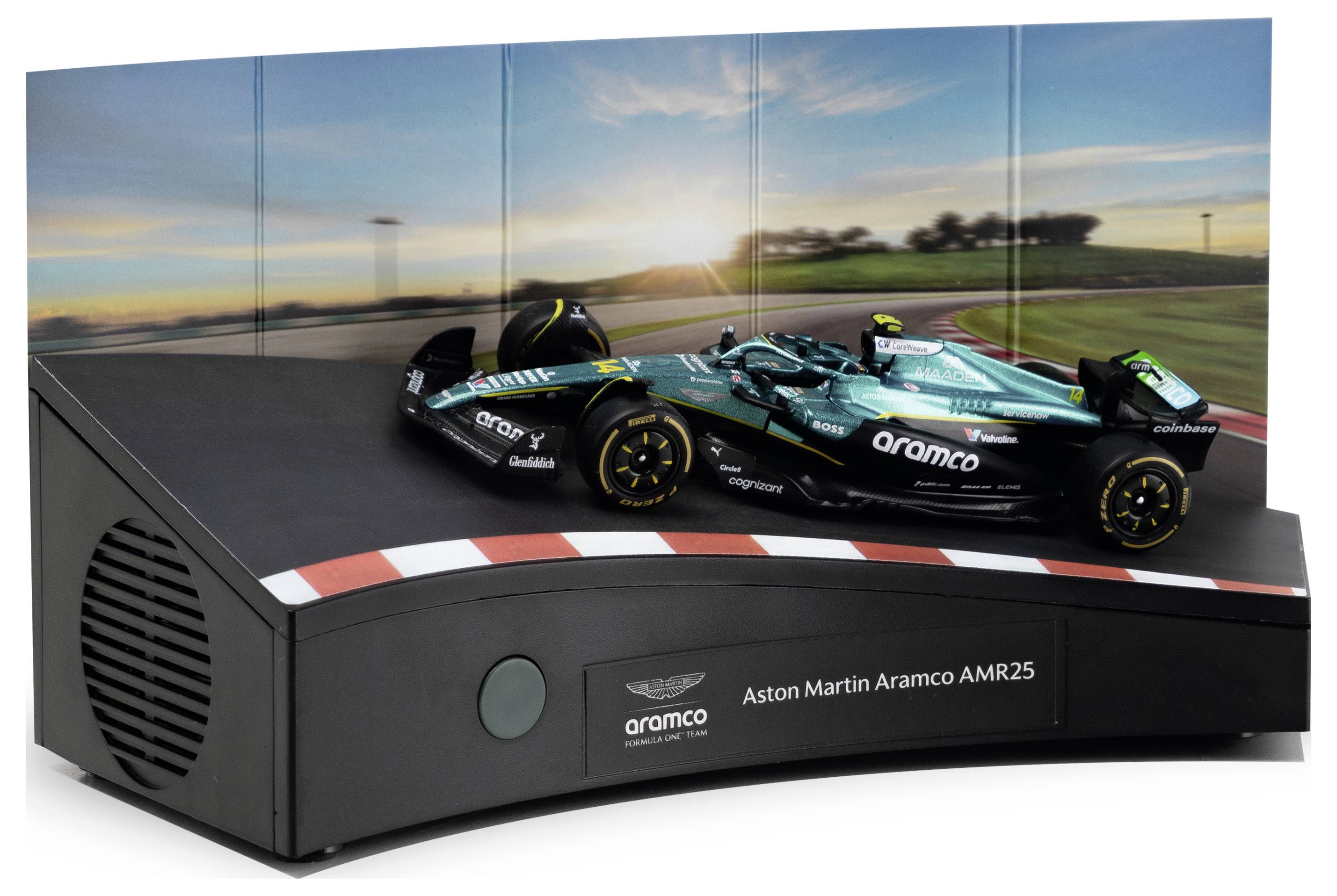 Aston Martin Aramco AMR25 Formel-1-Automodell im Maßstab, ausgestellt auf einem schwarzen Sockel mit einem Label „Aston Martin Aramco AMR25" vor einer Rennstrecken-Sonnenuntergang-Kulisse.