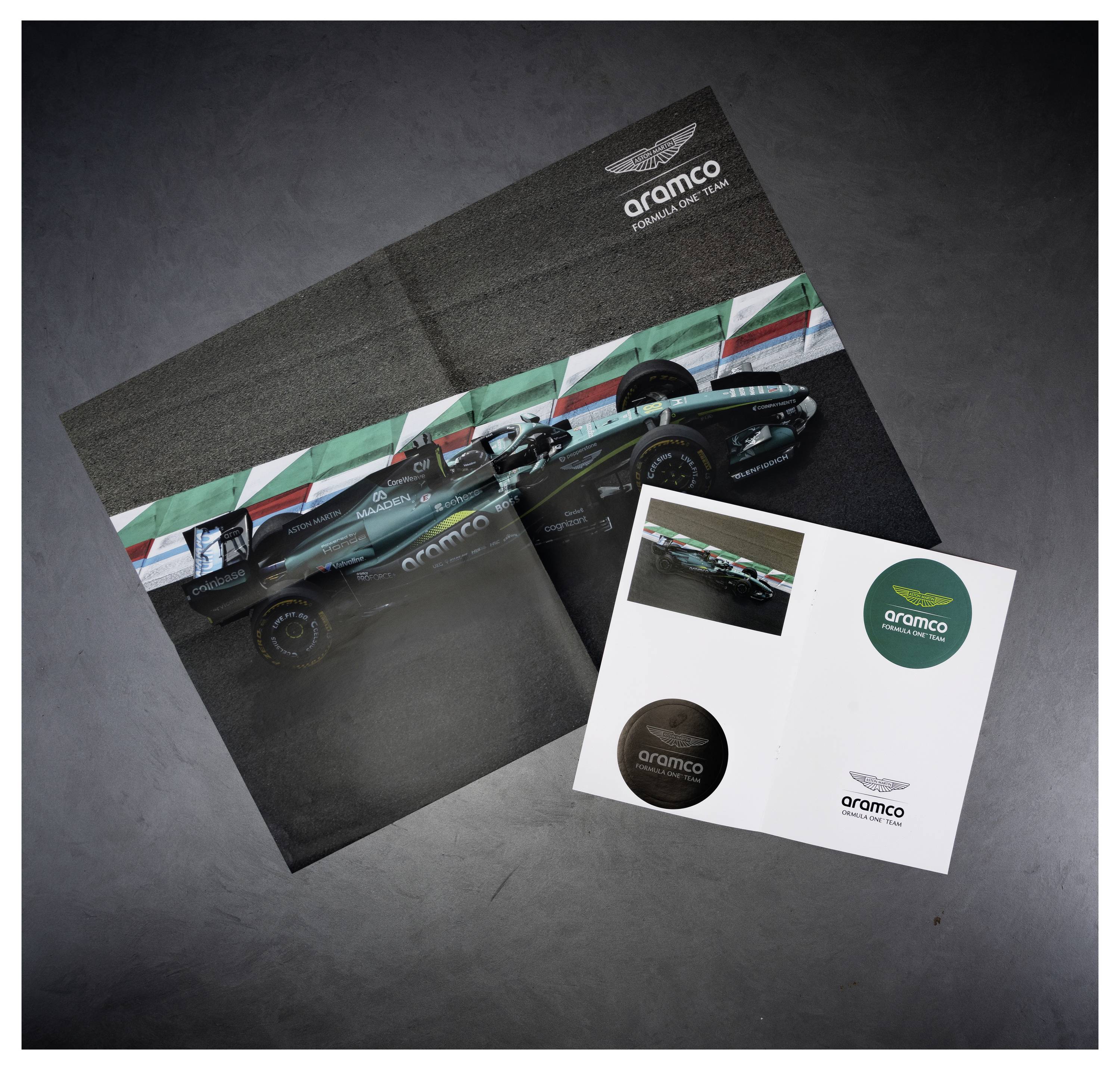 Ein Formula-1-Werbedruck-Set, bestehend aus einem Aramco-gebrandeten Rennwagen-Poster und passenden Logo-Aufklebern auf einer grauen Oberfläche.