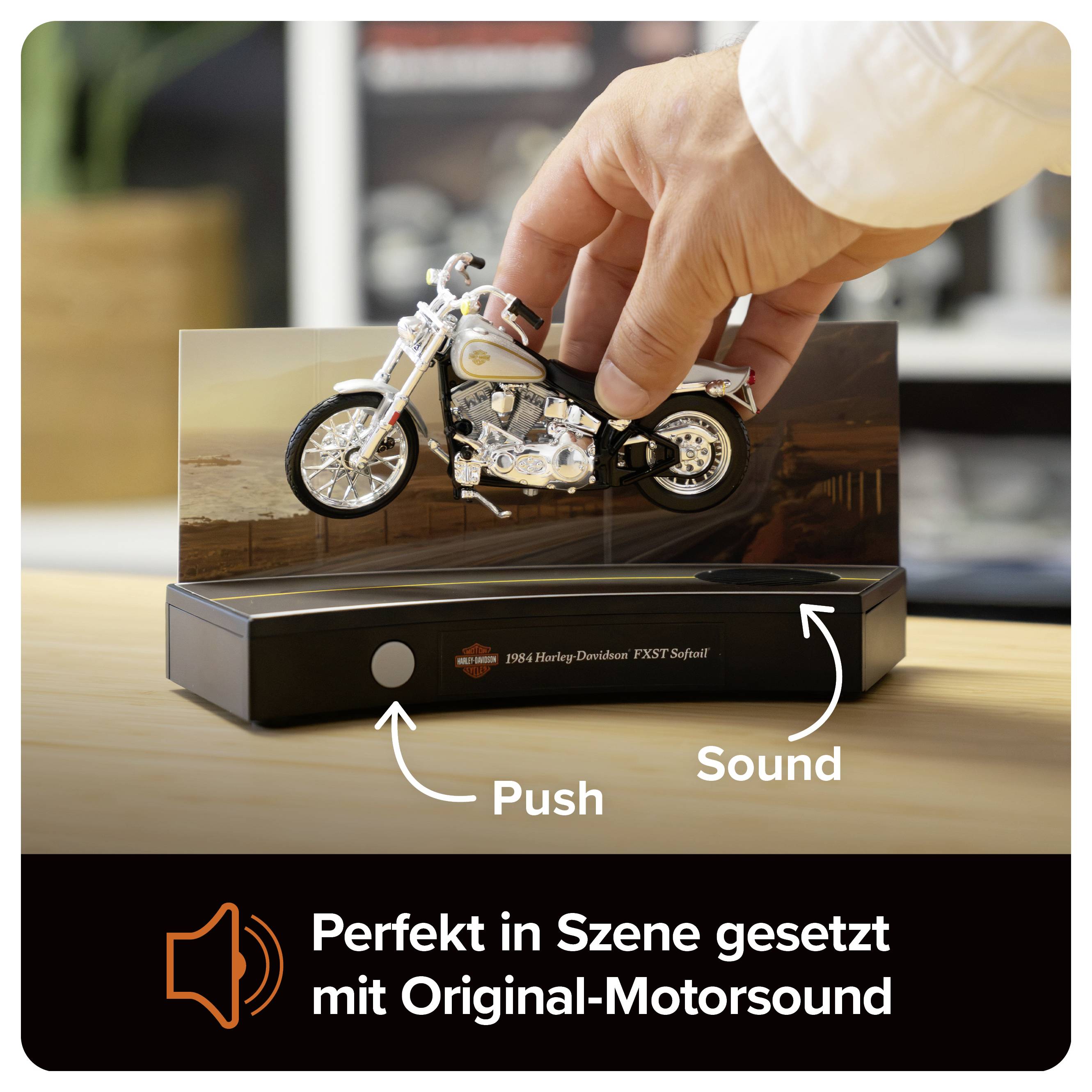 Hand drückt ein Harley-Davidson-Motorradmodell auf einer Präsentationsbasis; Beschriftung 'Push' und 'Sound', unten der Text 'Perfekt in Szene gesetzt mit Original-Motorsound'.