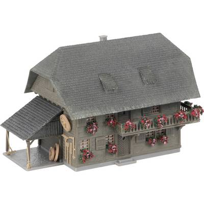 Holzmodell eines alpinen Hauses im Berghausstil mit steilem grauem Dach, Blumenkästen und einem kleinen Unterstand an der Seite.