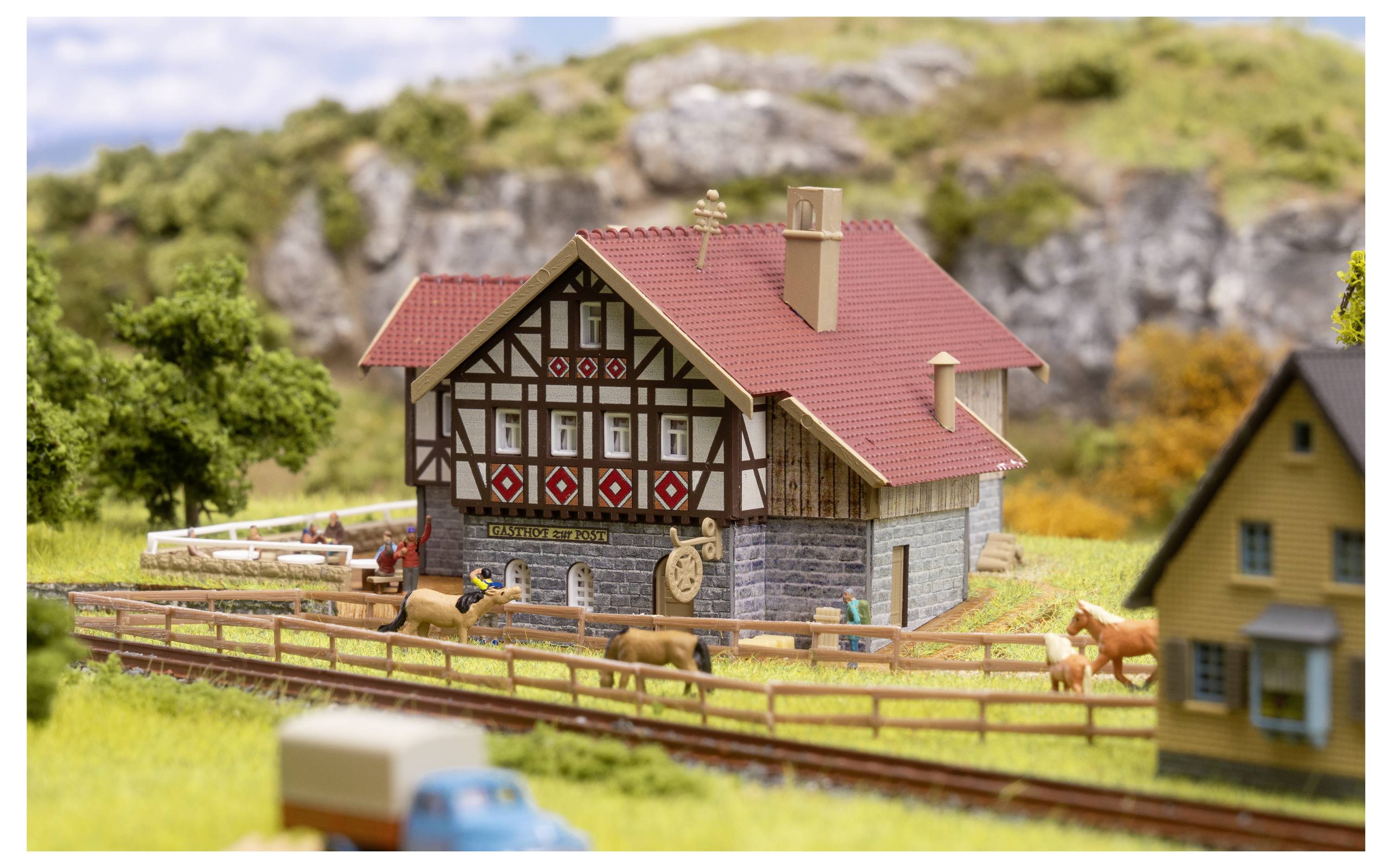 Modellfarm-Szenerie mit einem Fachwerkbauernhaus, eingezäunter Weide, Pferden und einem kleinen Lastwagen im Vordergrund.