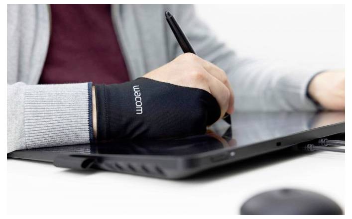 Nahaufnahme einer Person, die mit einem Stift auf einem Grafiktablett arbeitet, während sie einen Zeichenhandschuh trägt, mit einem Laptop in der Nähe.
