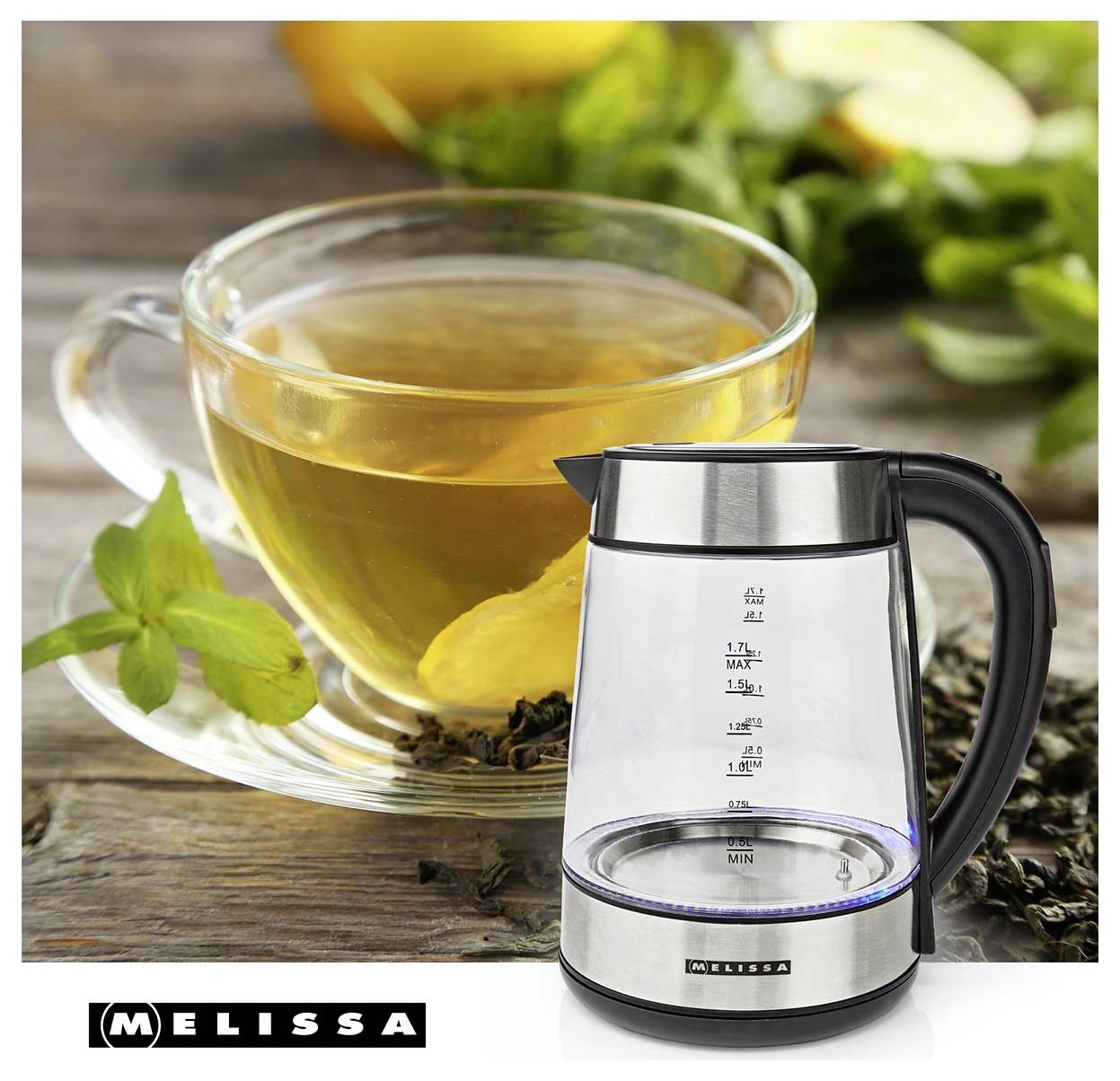 Glastasse mit heißem Tee, Zitrone und Minze neben einem elektrischen Wasserkocher von Melissa auf einem Holztisch, was auf Teezubereitung hindeutet.