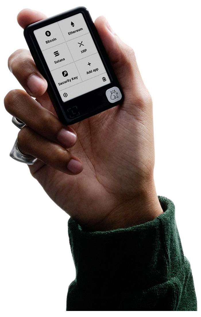 Hand hält einen kleinen quadratischen Smart-Controller, auf dem ein 2x3-Menü mit Optionen für Bitcoin, Ethereum, Solana, XRP, Wiederherstellungsphrase und App hinzufügen angezeigt wird.
