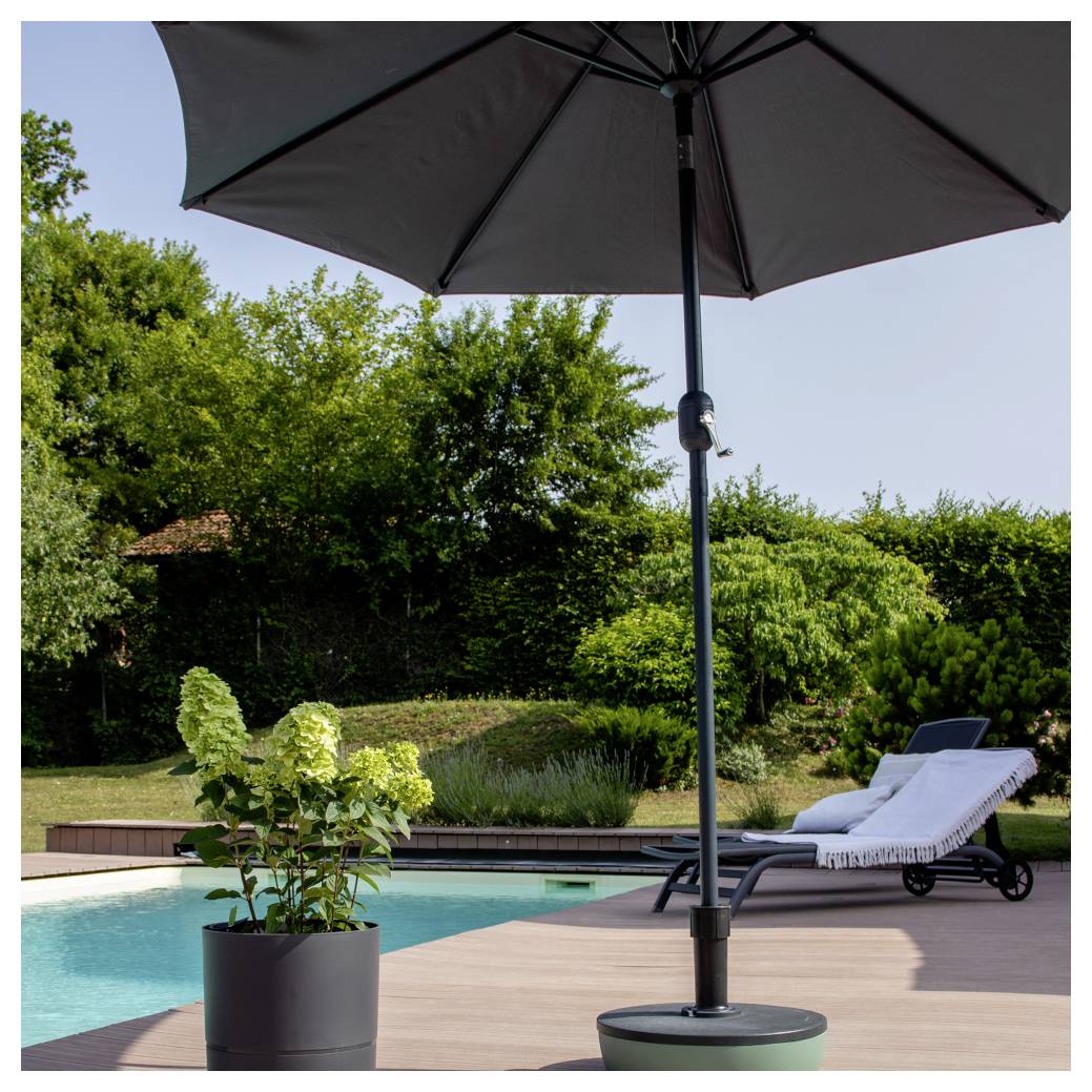 Hinterhof-Poolbereich mit großem schwarzem Sonnenschirm, Liegestuhl und Topfpflanze neben einem Schwimmbecken und grünem Garten.