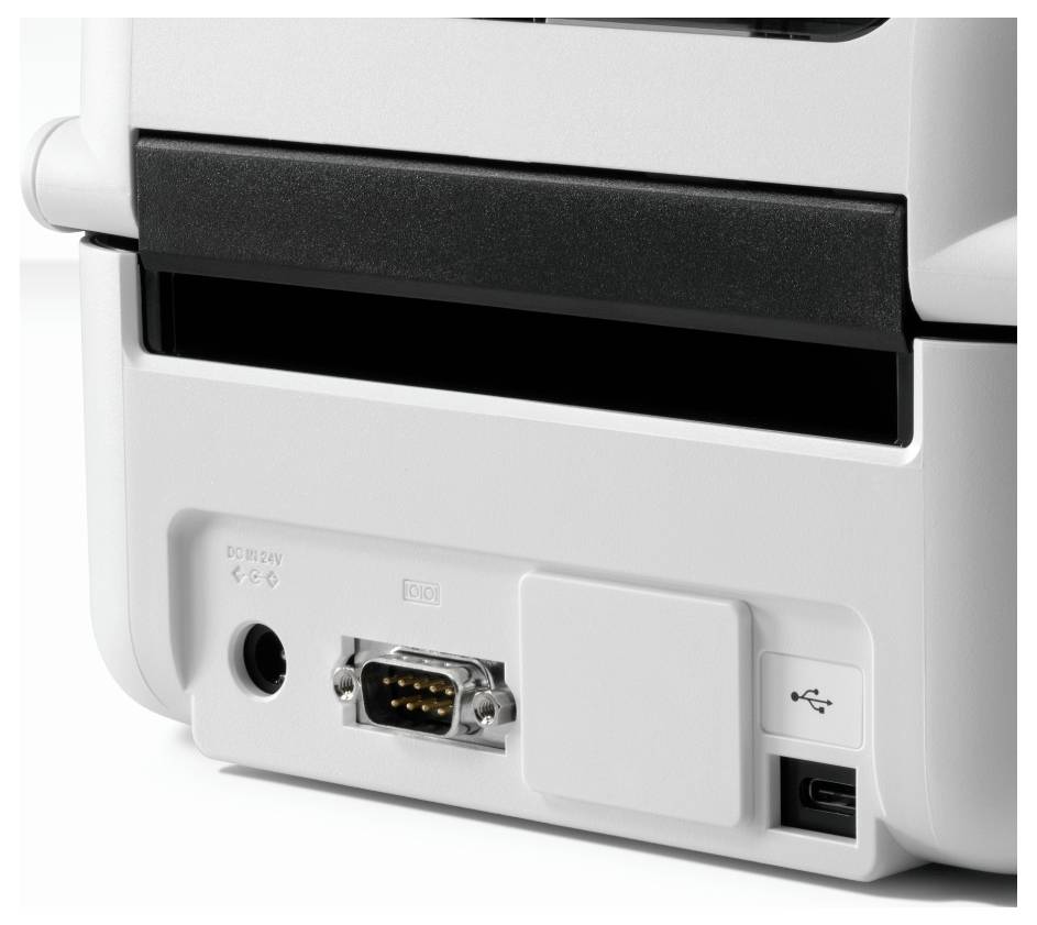 Nahaufnahme eines Anschlussfelds auf der Rückseite eines Geräts mit einer Stromanschluss-Buchse, einem seriellen Anschluss, einem USB-Anschluss und einem offenen Steckplatz auf einem weißen Kunststoffgehäuse.