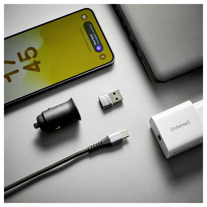 Smartphone, USB-C-Kabel, Ladegerät, Autoadapter und kabellose Ladezubehör auf einer grauen Oberfläche angeordnet.