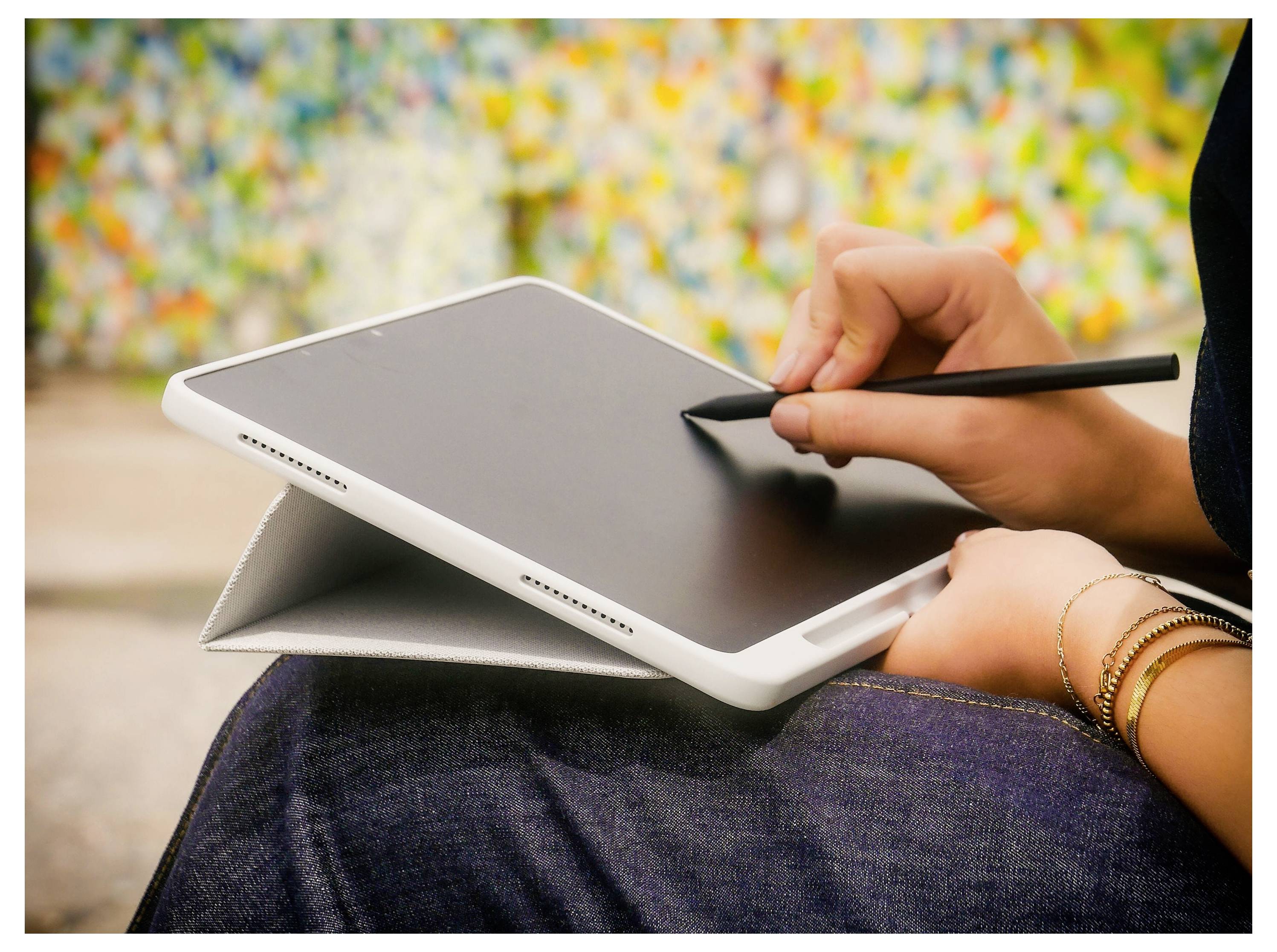 Eine Person, die einen Stift auf einem Tablet verwendet, das auf ihrem Schoß liegt, was auf digitales Zeichnen oder Notizen machen hindeutet.