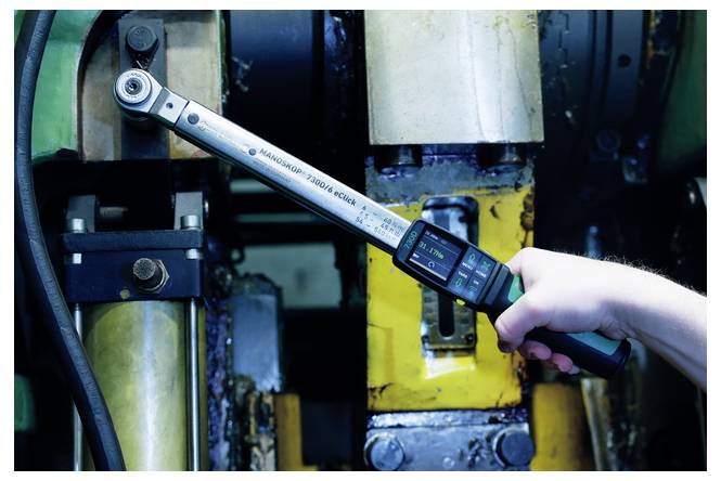 Eine Person verwendet einen digitalen Drehmomentschlüssel zum Anziehen von Bolzen an Industriemaschinen in einer Werkstatt.