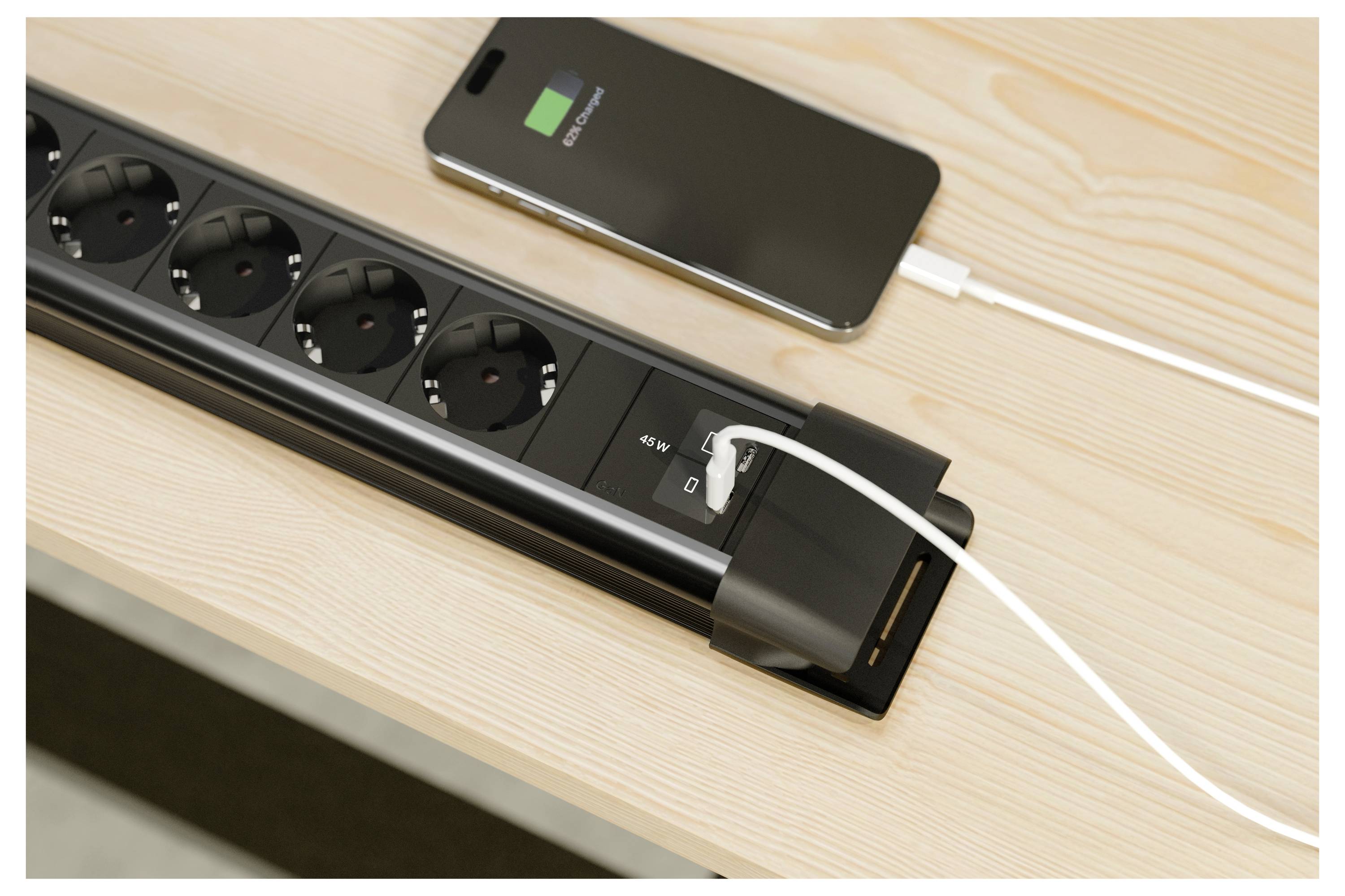 Steckerleiste mit mehreren Steckdosen und USB-Anschlüssen auf einem Schreibtisch, die ein Smartphone mit einem weißen Kabel auflädt.