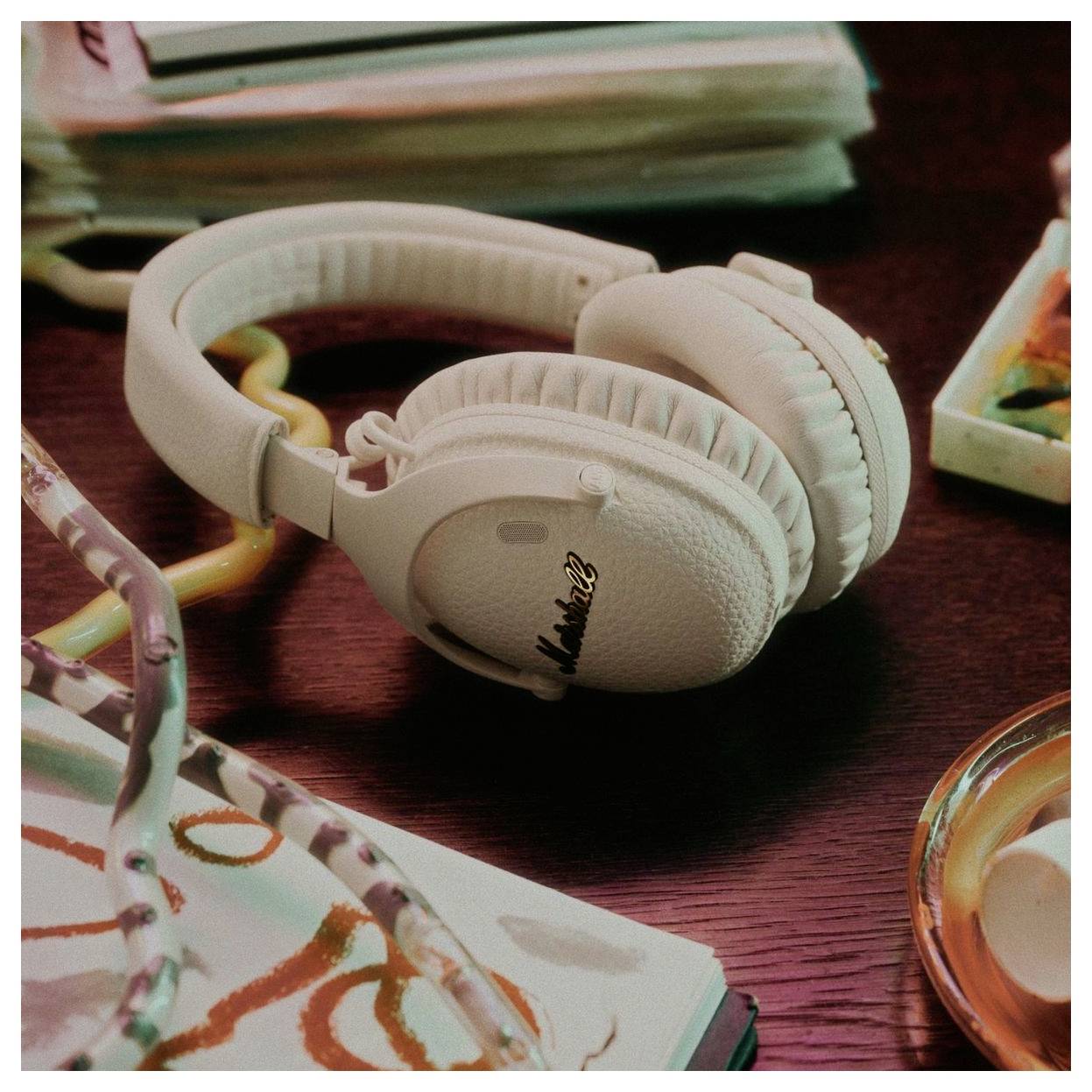 Weiße Marshall-Over-Ear-Kopfhörer, die auf einem Schreibtisch neben Notizbüchern und einer Kerze ruhen