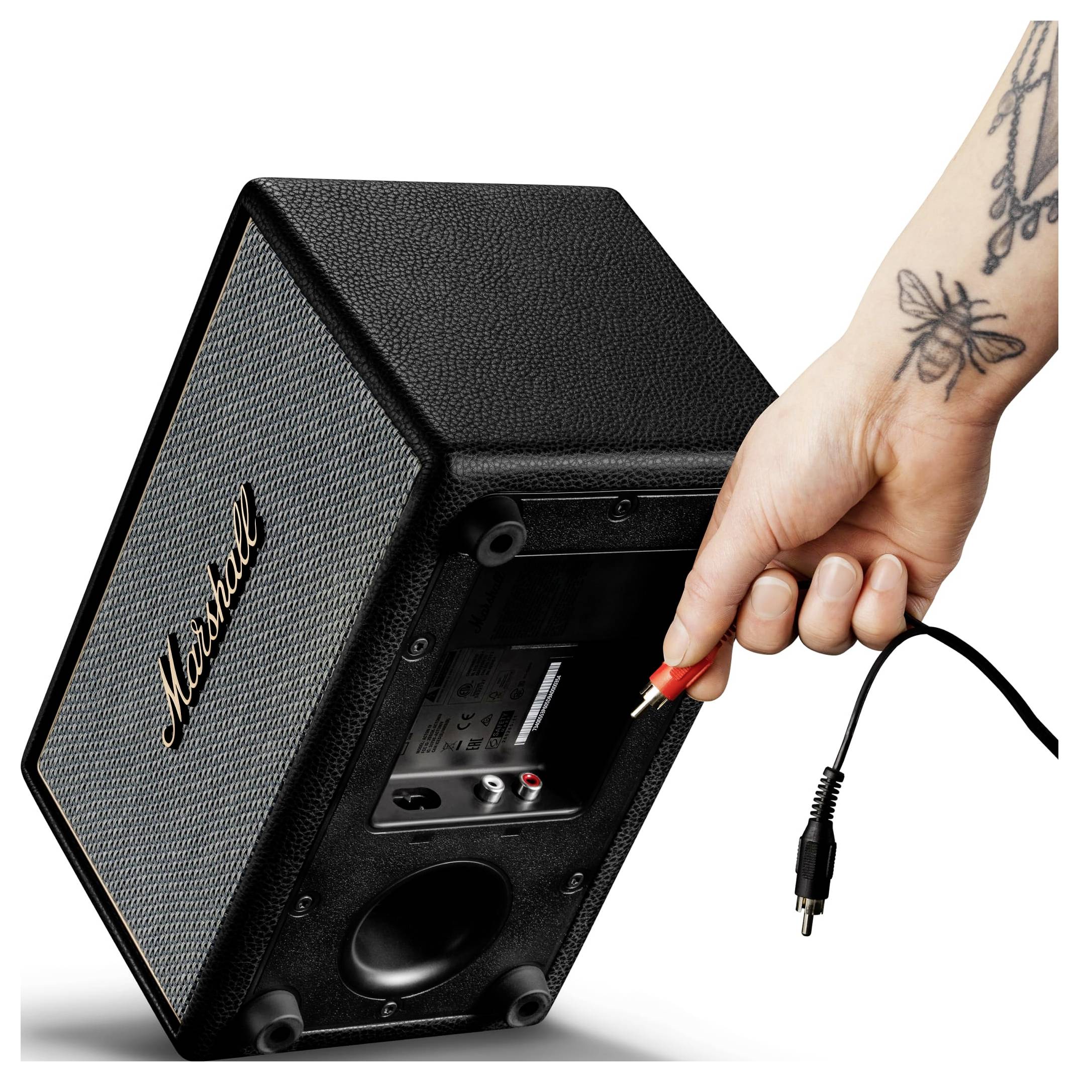 Hand steckt einen roten Audiostecker in die Rückseite eines Marshall-Lautsprecherschranks, wobei der Lautsprecher so angewinkelt ist, dass sein Eingangsfeld sichtbar ist.