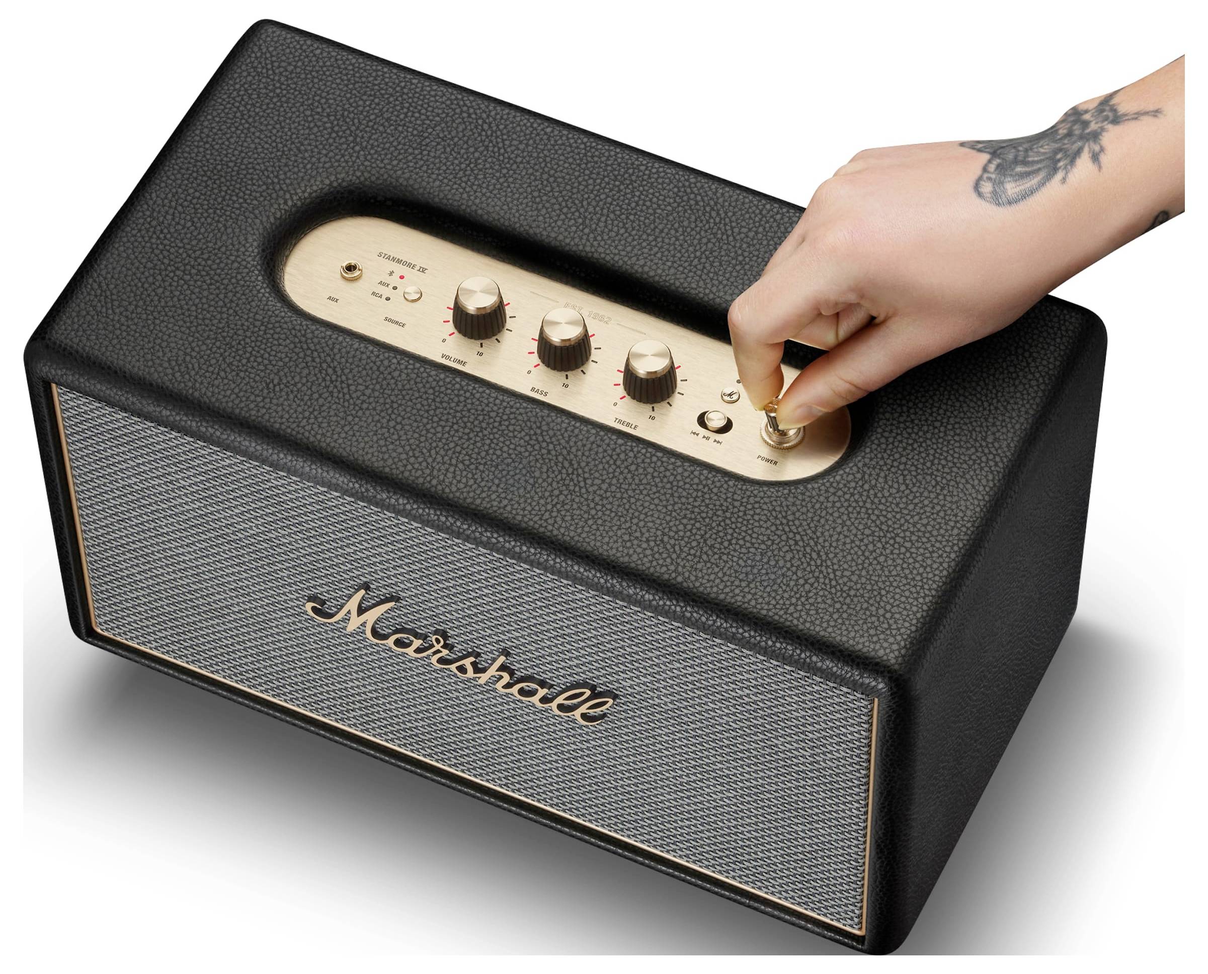 Eine Hand dreht den Stromknopf an einem Marshall-Lautsprecher, von oben fotografiert vor weißem Hintergrund.