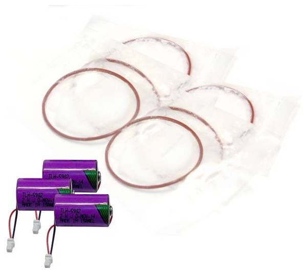 Drei violette Lithiumbatterien und mehrere transparente Klebstoffringe oder -pads auf weißem Hintergrund.
