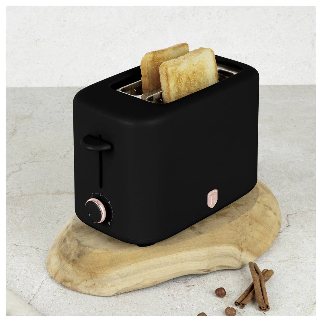 Schwarzer Zwei-Scheiben-Toaster mit hochspringendem Toast, sitzt auf einem Holzbrett mit Zimtstangen auf einer hellen Arbeitsplatte.