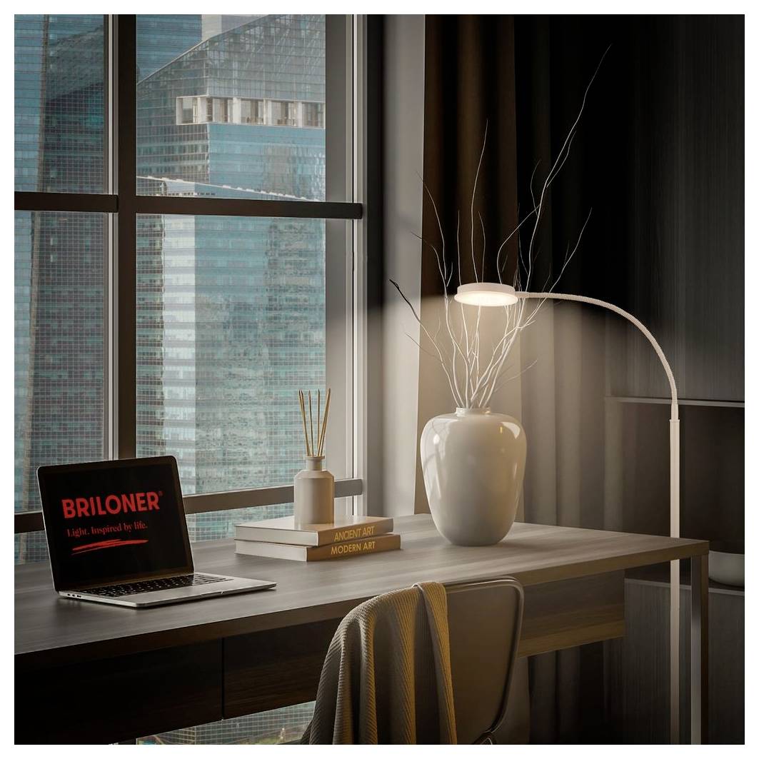 Moderner Schreibtisch-Arbeitsplatz an einem Fenster mit Laptop, auf dem "BRILONER" angezeigt wird, Bücher, eine Vase und eine leuchtende Lampe in einer Hochhausumgebung.