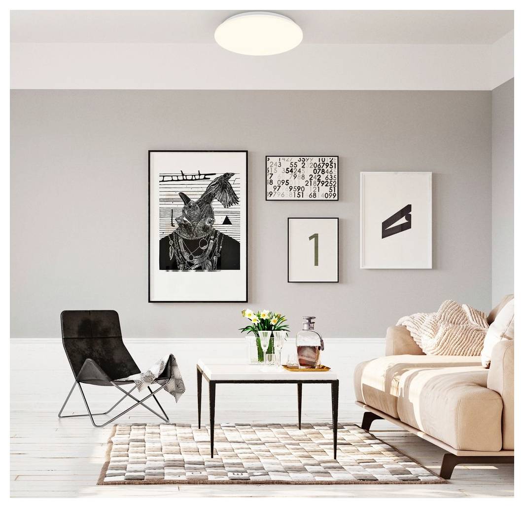 Modernes Wohnzimmer mit beigem Sofa, schwarzem Loungesessel, Couchtisch, gemustertem Teppich und rahmenlosem Wandbild an einer grauen Wand.