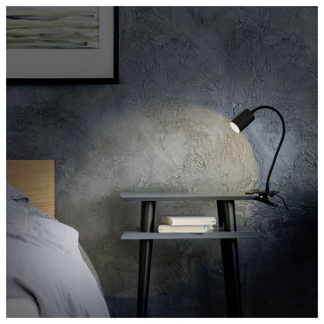 Nachttisch mit einer leuchtenden verstellbaren Lampe, die Licht auf eine strukturierte Wand neben einem Bett wirft, mit einem kleinen Bücherstapel darunter.