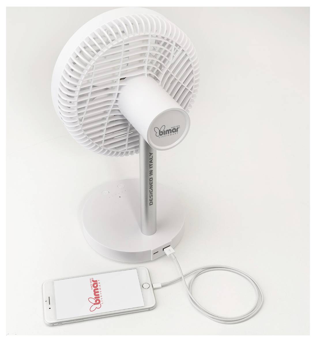 Tragbarer weißer Ventilator auf einem Ständer, der über ein Kabel mit einem Smartphone verbunden ist und USB-Stromversorgung oder Ladefunktion andeutet.