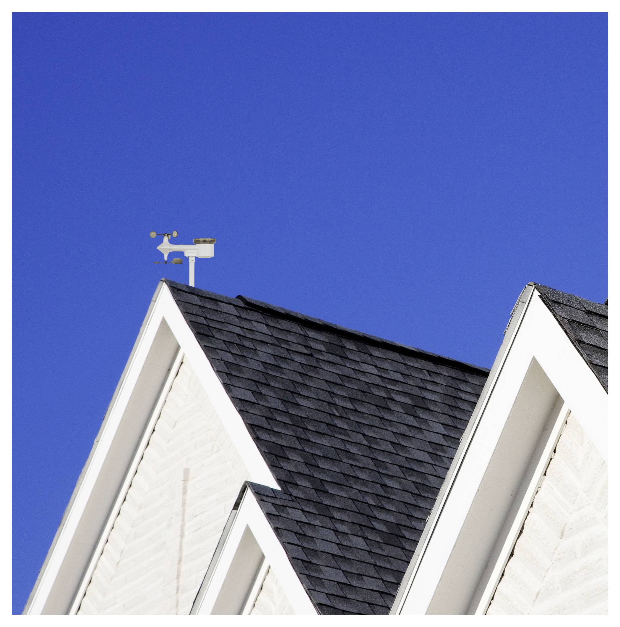Zwei Hausgiebel mit dunklen Schindeldächern vor einem klaren blauen Himmel, mit einer Wetterfahne auf dem linken Dachfirst.