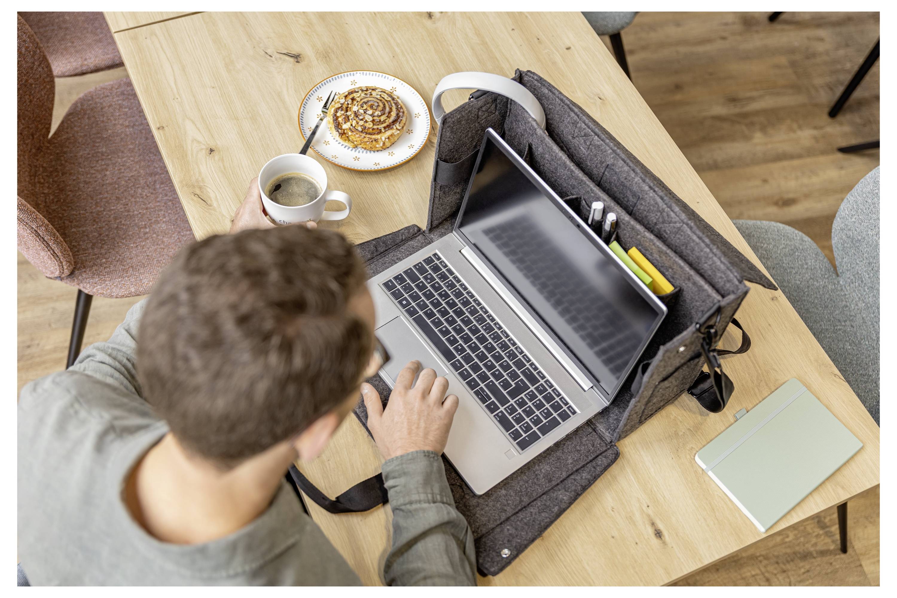 Vogelperspektive einer Person, die an einem Laptop an einem Holztisch arbeitet, mit Kaffee, Gebäck und einem Notizbuch