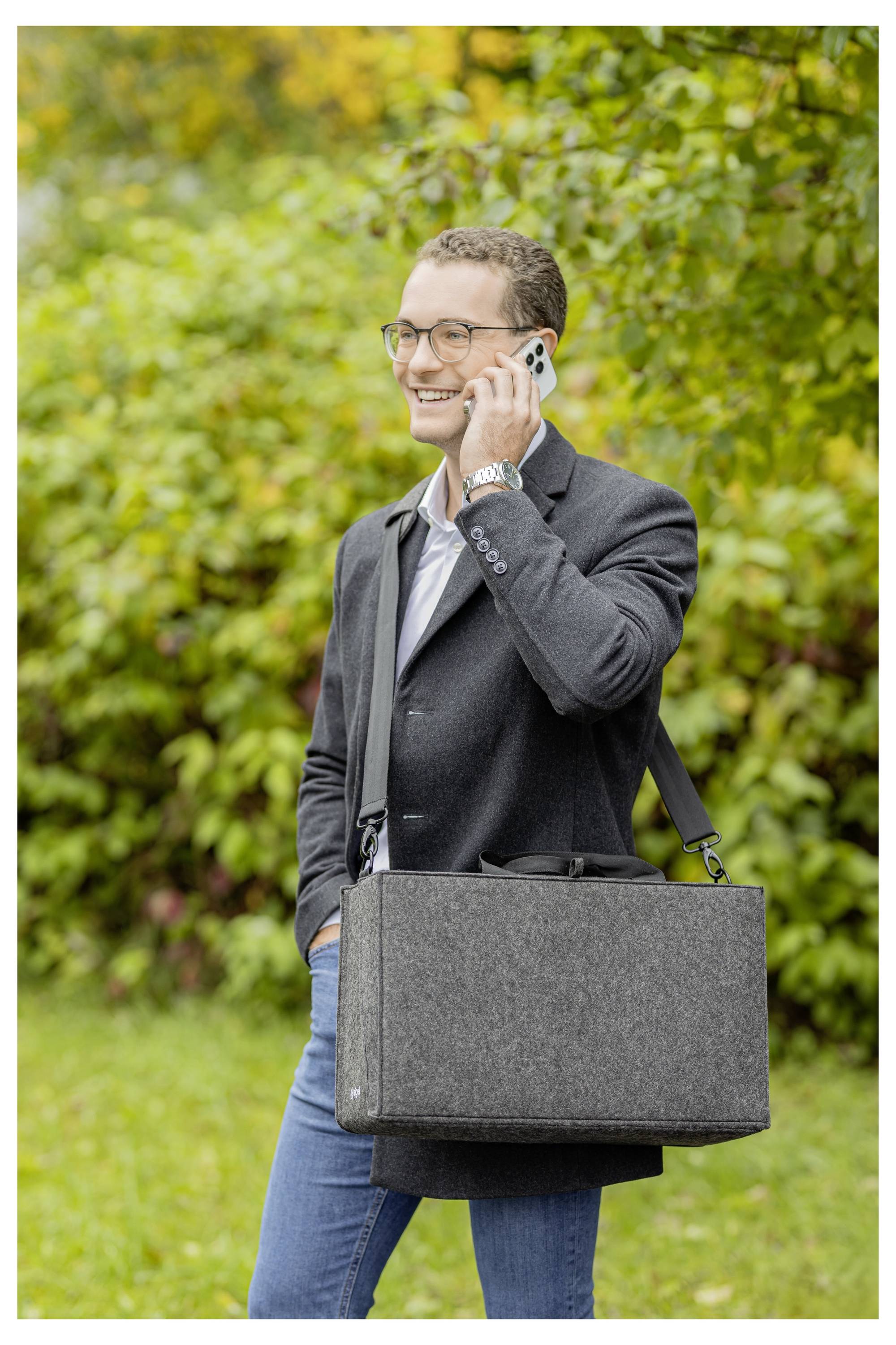 Ein lächelnder Mann in einem Blazer telefoniert im Freien und trägt eine graue Aktentasche über der Schulter.