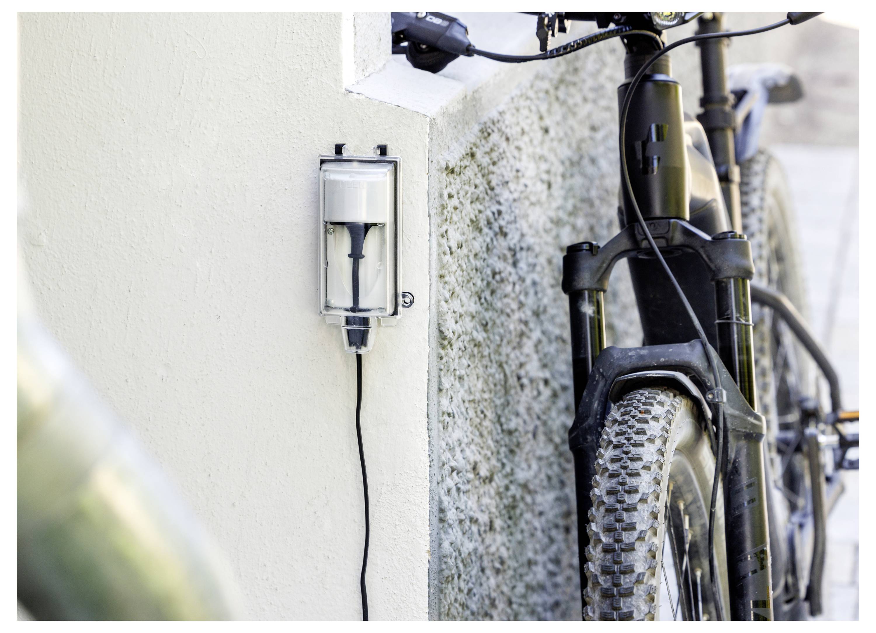 Wandmontierte E-Bike-Ladestation neben einem geparkten Mountainbike mit angeschlossenem Ladekabel.