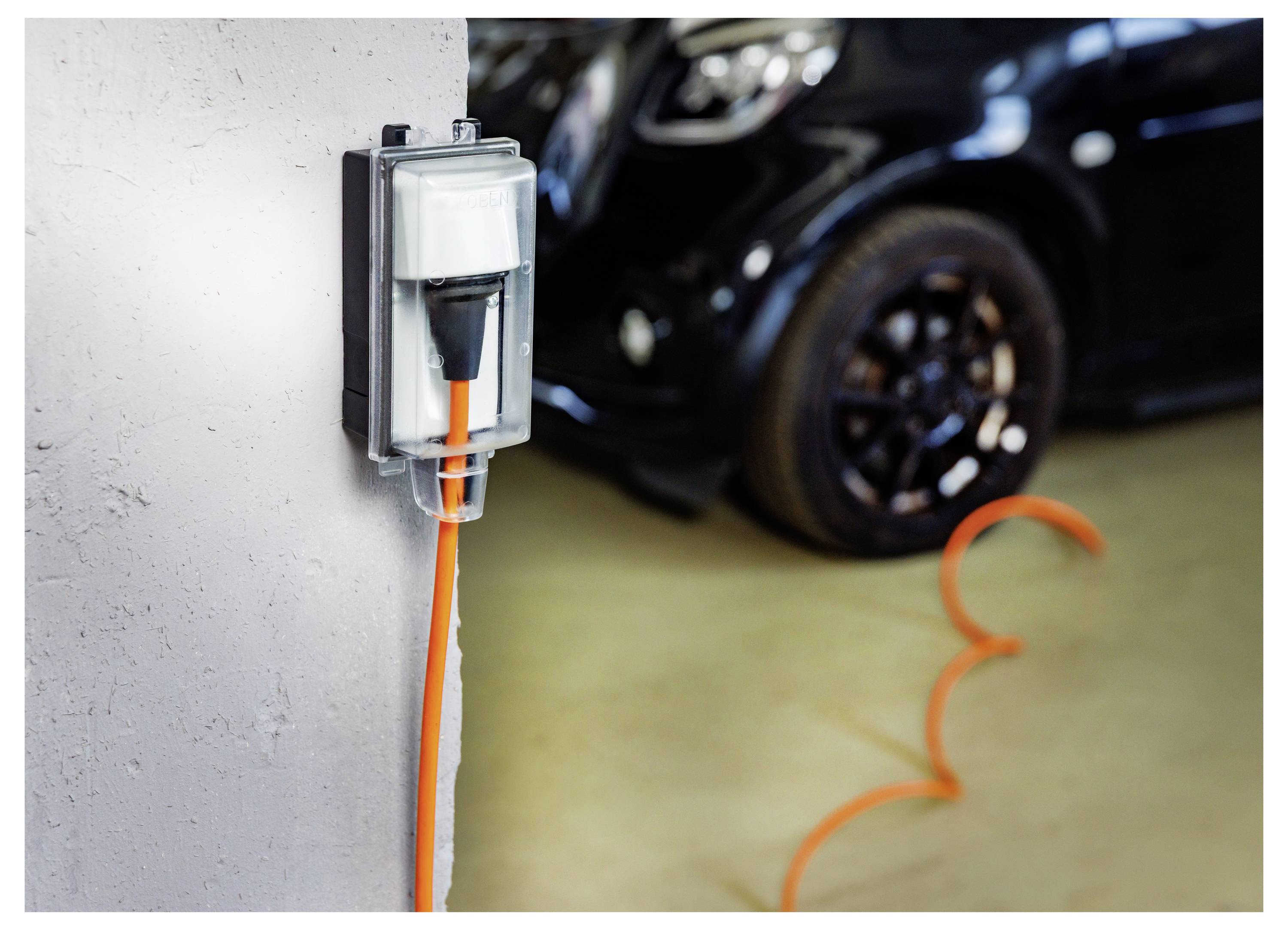 Ladestecker für Elektrofahrzeuge an der Wand montiert, mit einem orangefarbenen Kabel, das zu einem geparkten Auto in einer Garage führt.