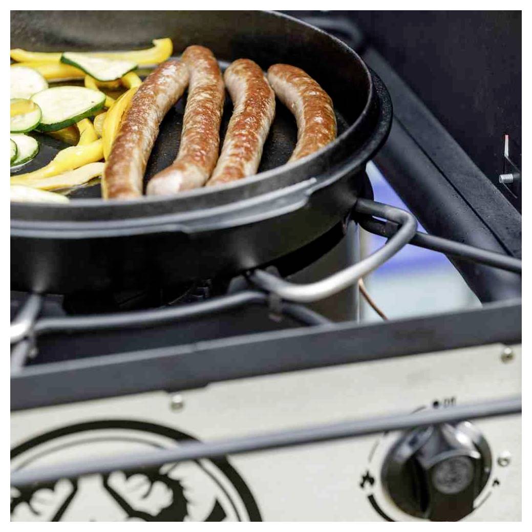 Würstchen und geschnittenes Gemüse, das in einer Pfanne auf einem Gasbrenner kocht, mit sichtbarem Grillreglerkopf darunter.
