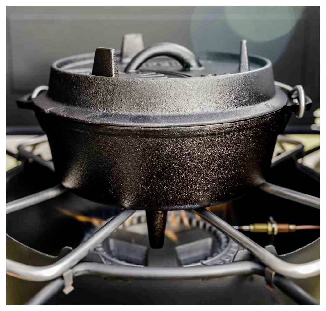 Gusseiserner Dutch Oven wird auf einem Gasflammkocher mit sichtbarer Flamme darunter erhitzt.