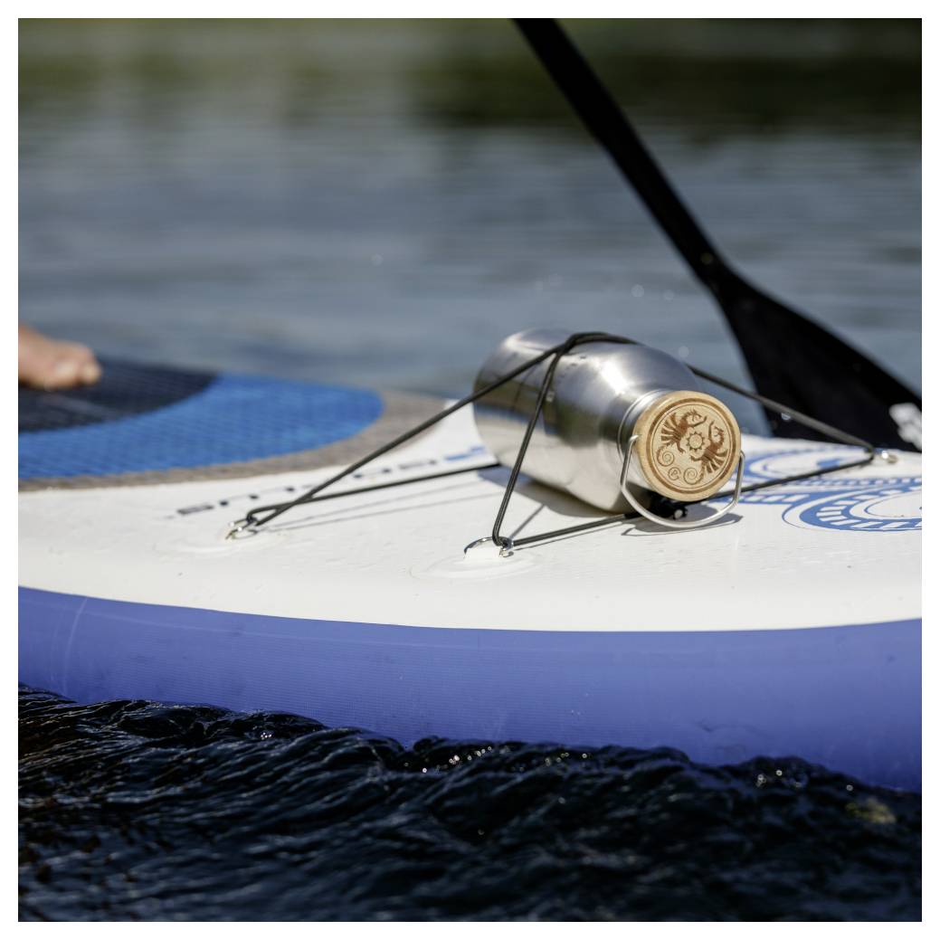 Metallische Wasserflasche, an dem Deck eines Paddleboards befestigt, das auf ruhigem Wasser schwimmt.