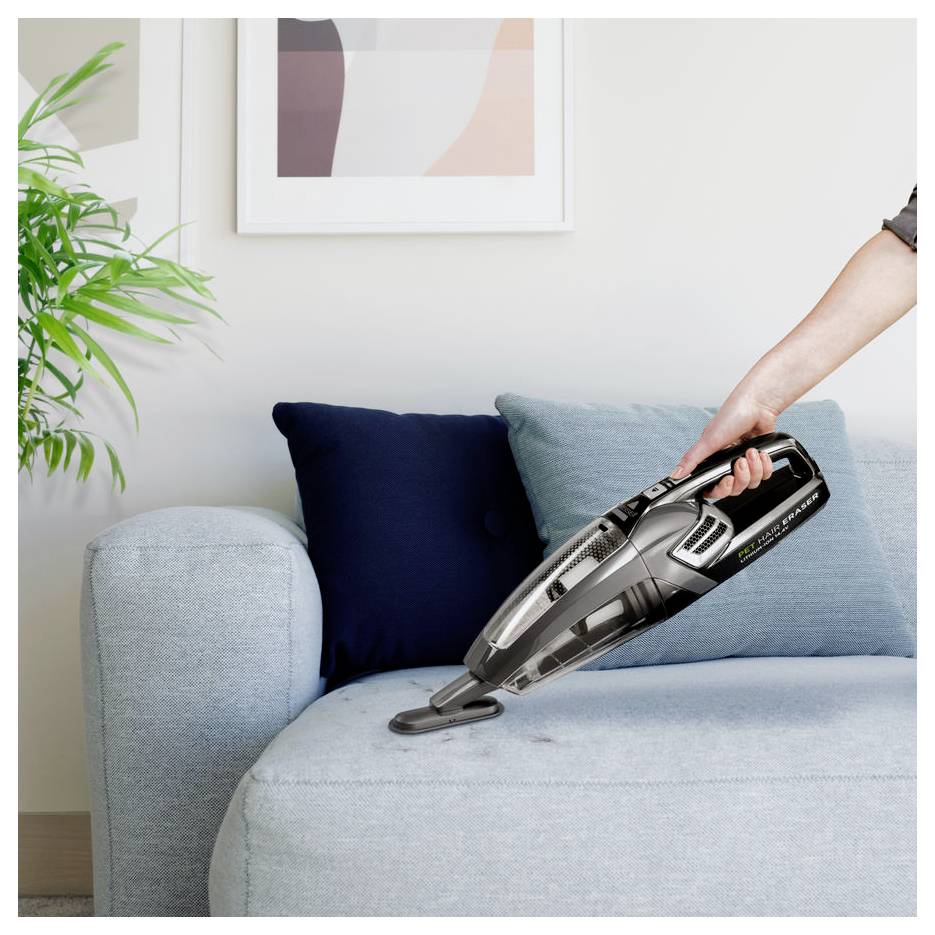 Ein tragbarer kabelloses Staubsauger reinigt ein hellblaues Sofa in einem Wohnzimmer.