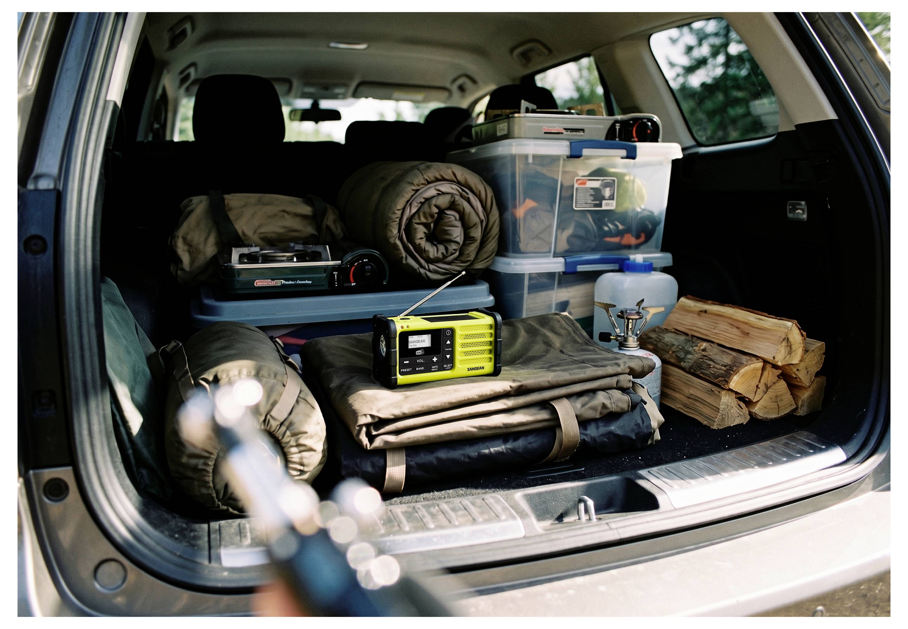 Offener Kofferraum eines Autos, gepackt mit Campingausrüstung: aufgerollte Schlafsäcke, Lagerkisten, tragbares Radio, gefaltete Matten und Brennholz.