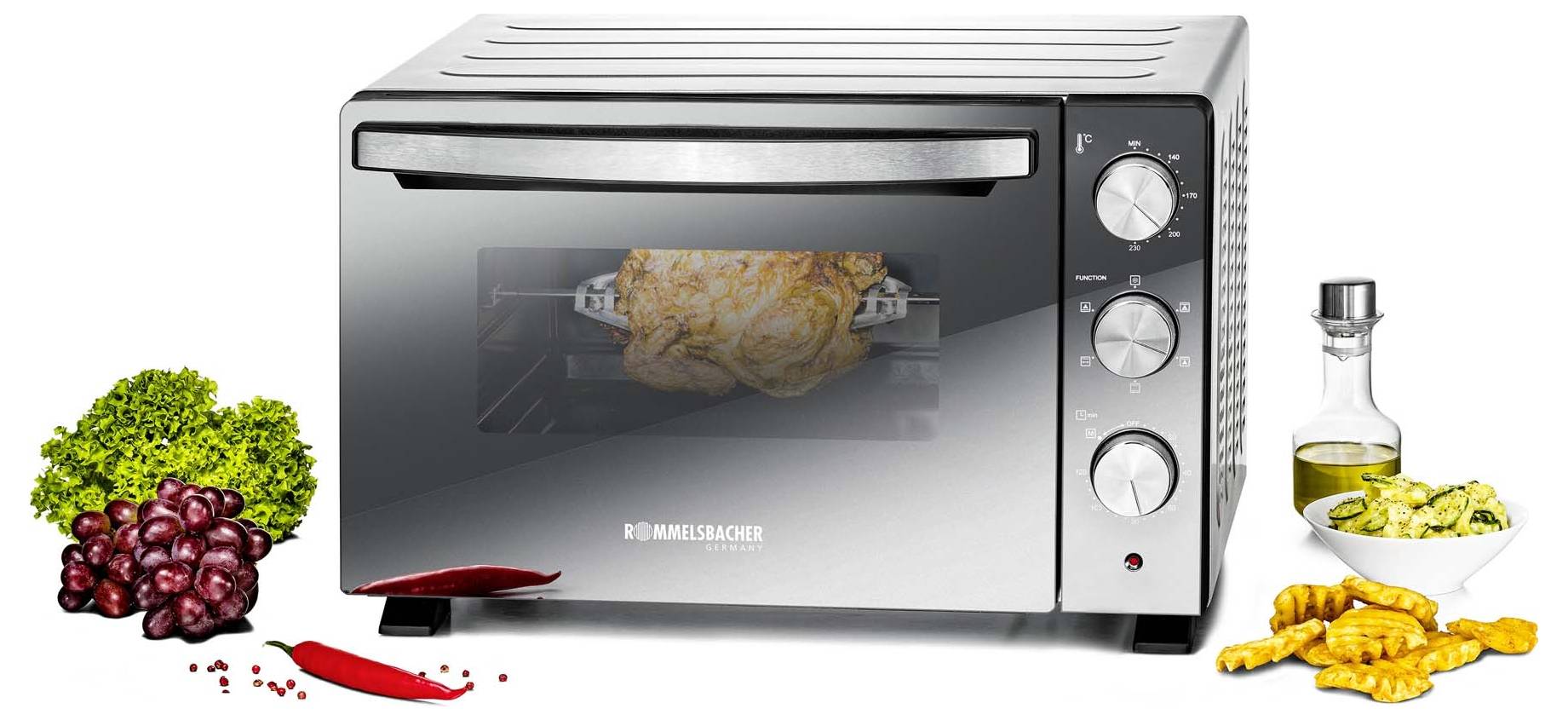 Küchenarbeitsplatte-Toasterofen mit Hähnchen, das auf einem Spieß geröstet wird, mit Gemüse, Weinflasche und gabelzartem Essen, das herum angerichtet ist.