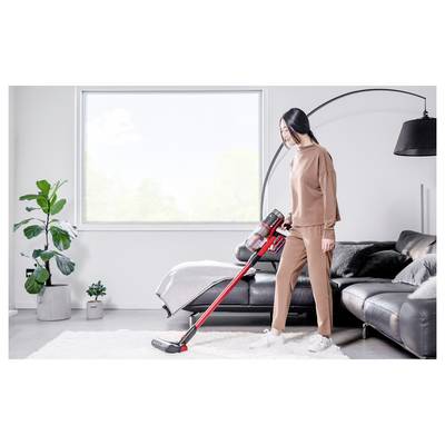 Frau staubsaugt einen weißen Teppich in einem hellen Wohnzimmer neben einem schwarzen Sofa und einer Stehlampe.