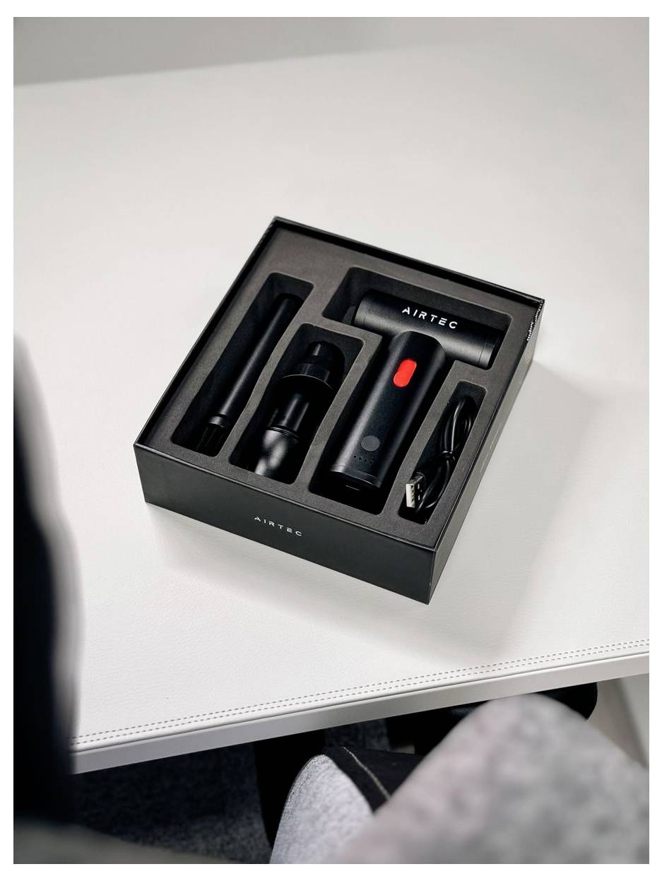 Ein AIRTEC-Akku-Werkzeugsatz in einer schwarzen Präsentationsbox auf weißem Tisch, mit dem Griff, den Aufsätzen und dem Ladekabel ordentlich angeordnet.