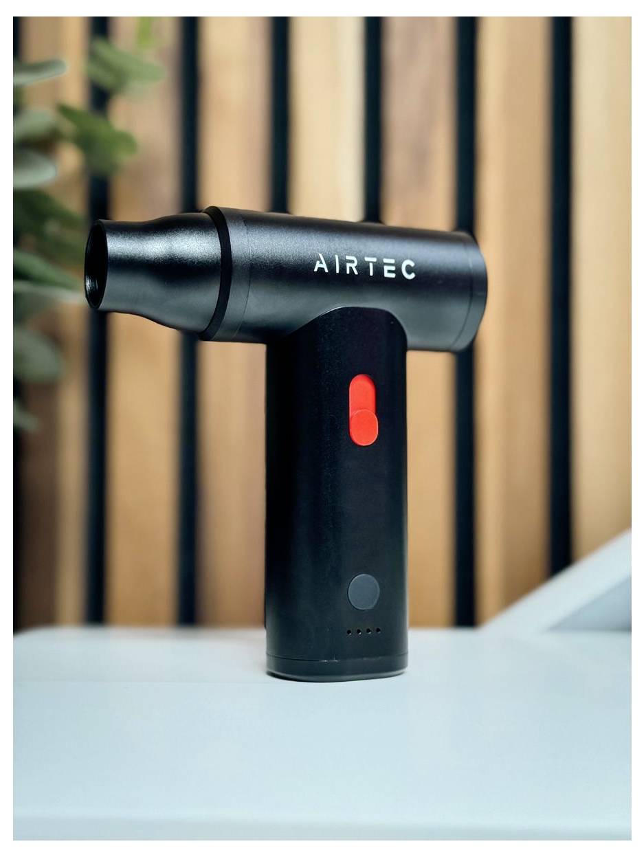 Schwarzes tragbares AIRTEC-Gerät mit rotem Netzschalter, das auf einer weißen Oberfläche vor einem unscharfen Holzhintergrund steht.