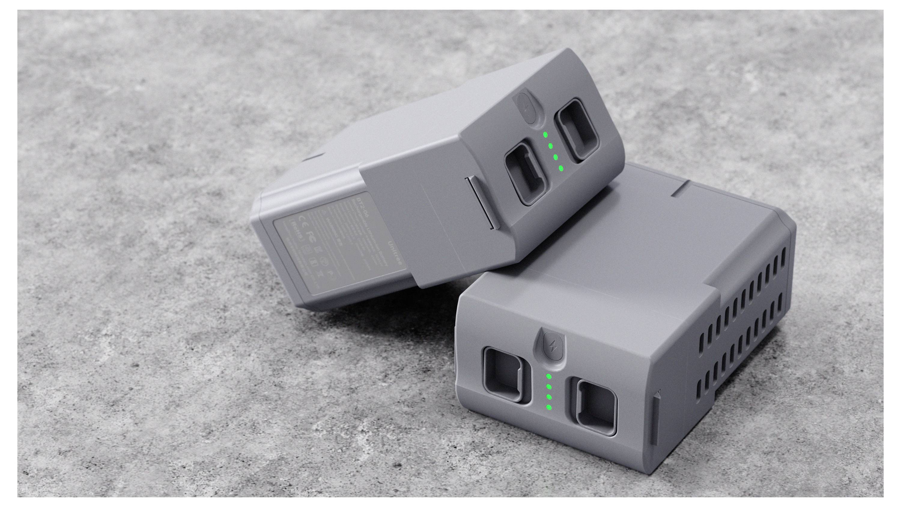 Zwei graue wiederaufladbare Batteriepacks auf einer Betonoberfläche, jedes mit einem Ladeanschluss und grünen Kontrollleuchten.