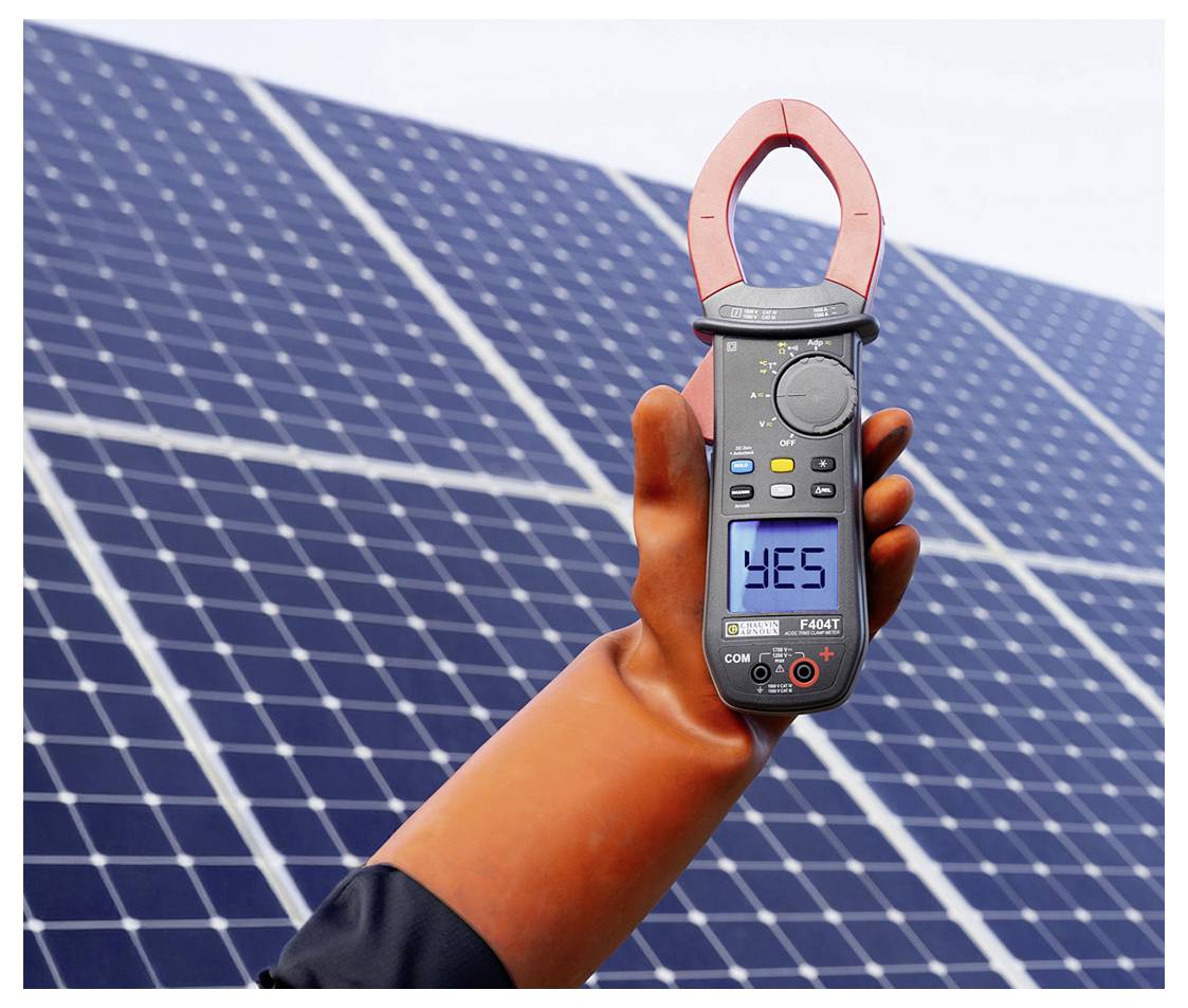Hand, die ein digitales Zangenprüfgerät vor Solarpaneelen hält, wobei das Display "JA" anzeigt.