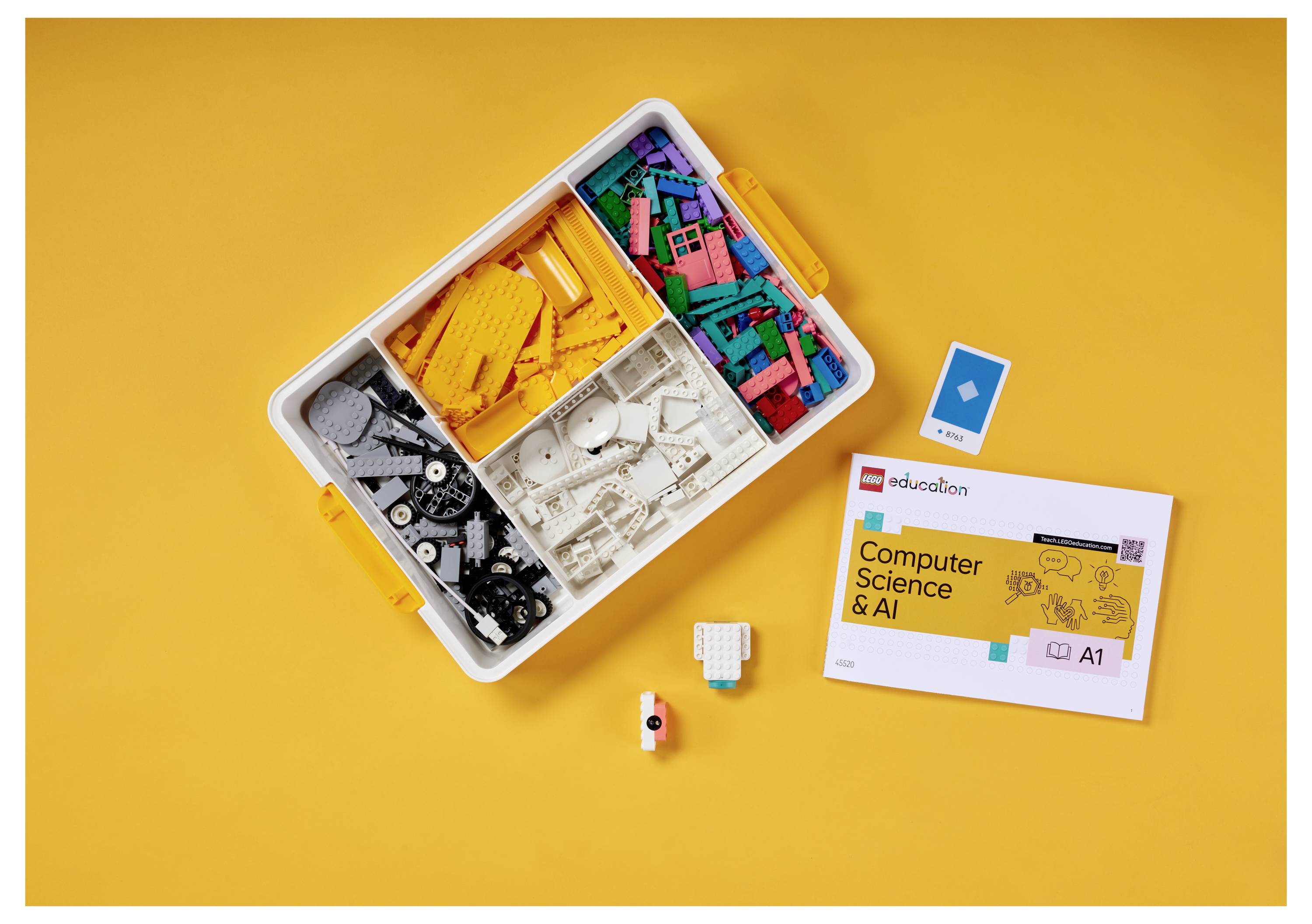 LEGO Education "Computer Science & AI"-Set mit einem Teileablagefach, einem Anleitungsheft und einigen losen Teilen auf gelbem Hintergrund.